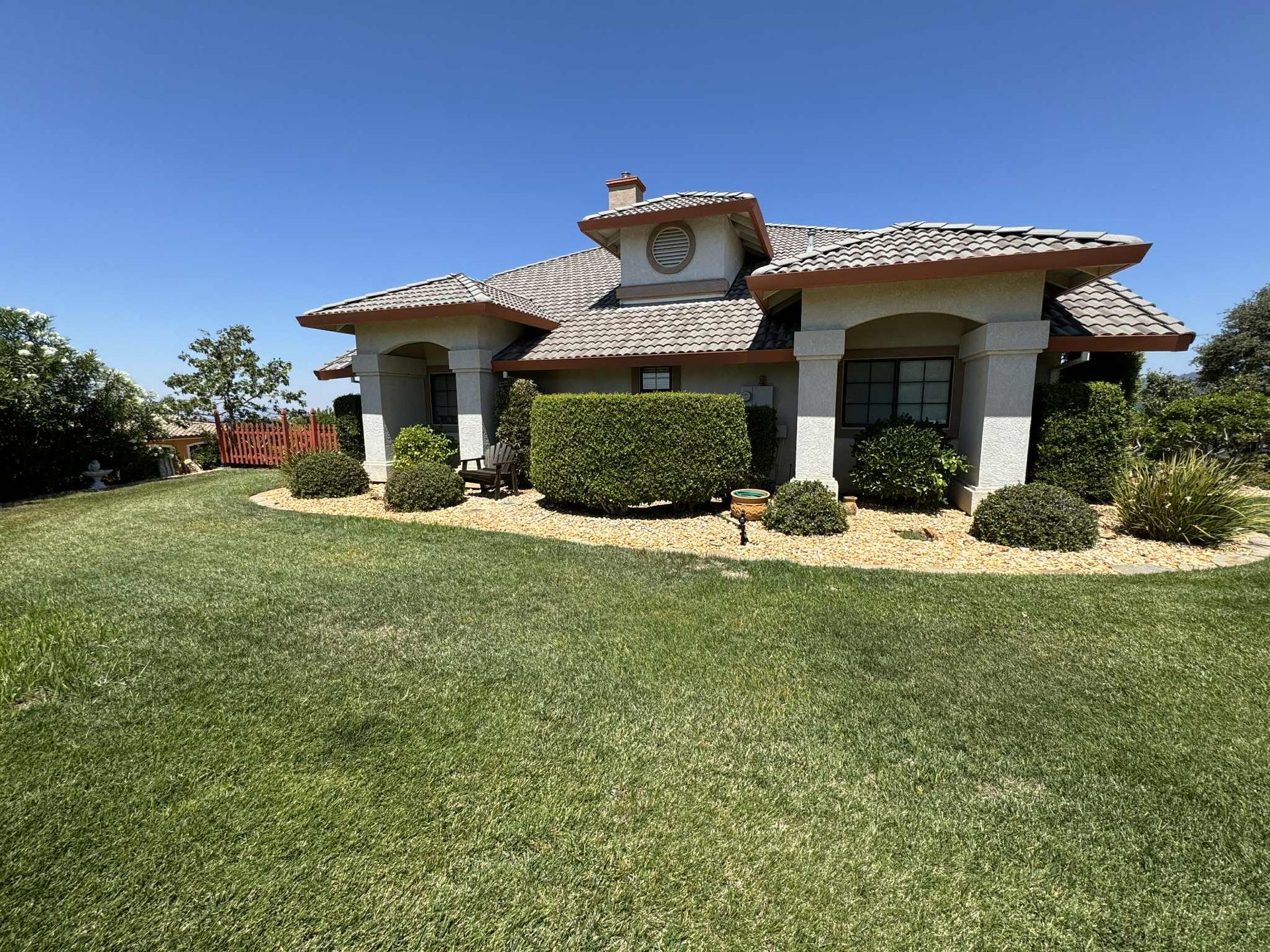 House with light stucco, brown roof tiles, green lawn, blue sky.