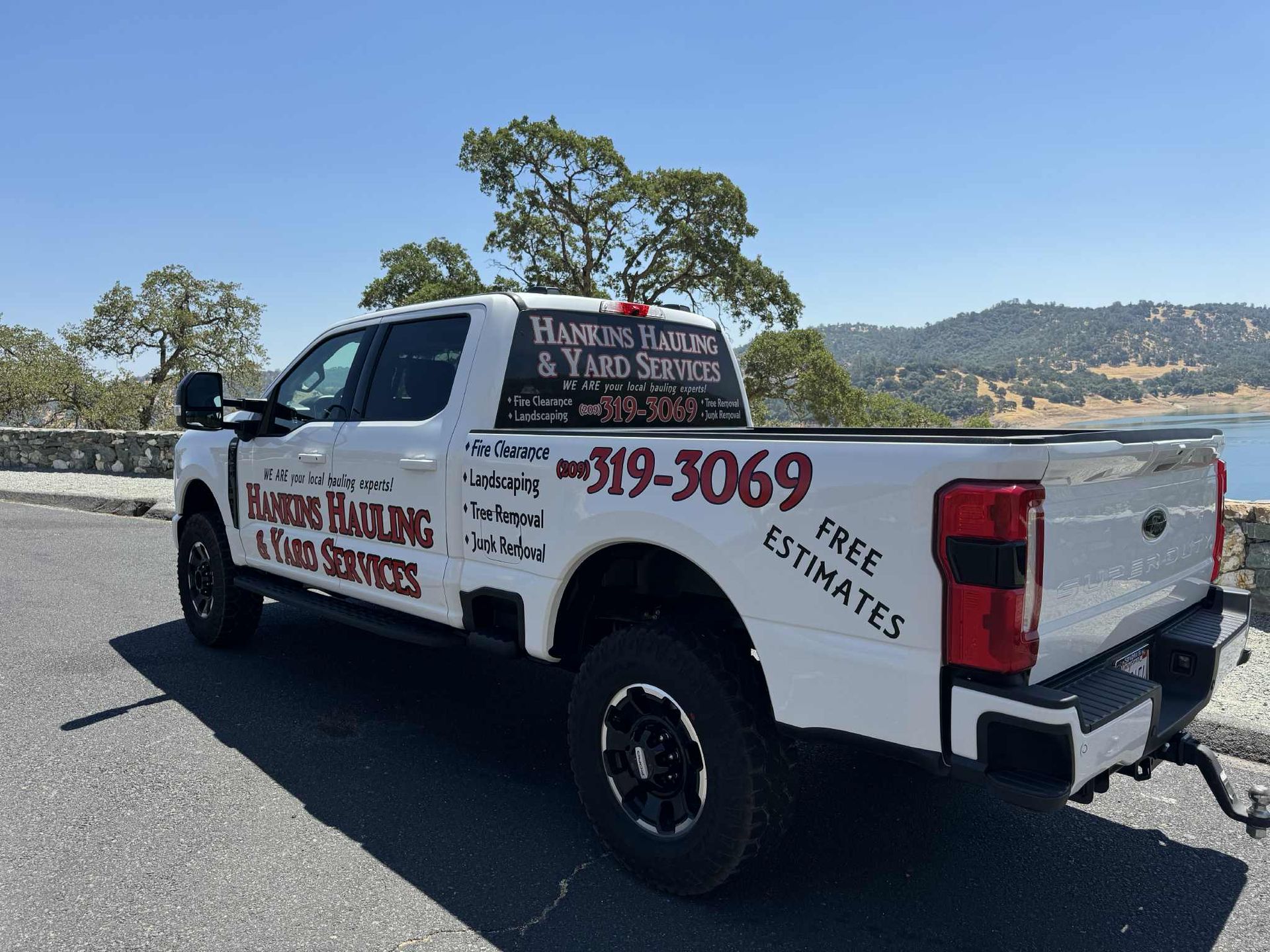 White truck with Hamburg Hauling & Yard Services logo, parked by a lake.
