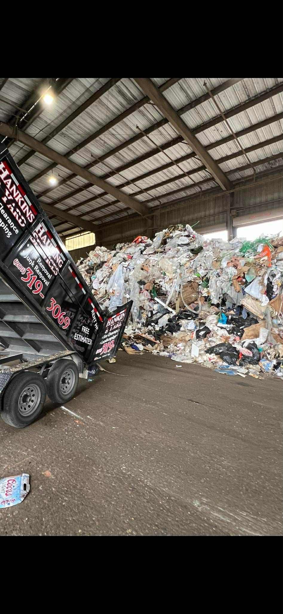 A truck dumping trash at a recycling center; inside a large building with metal roof.