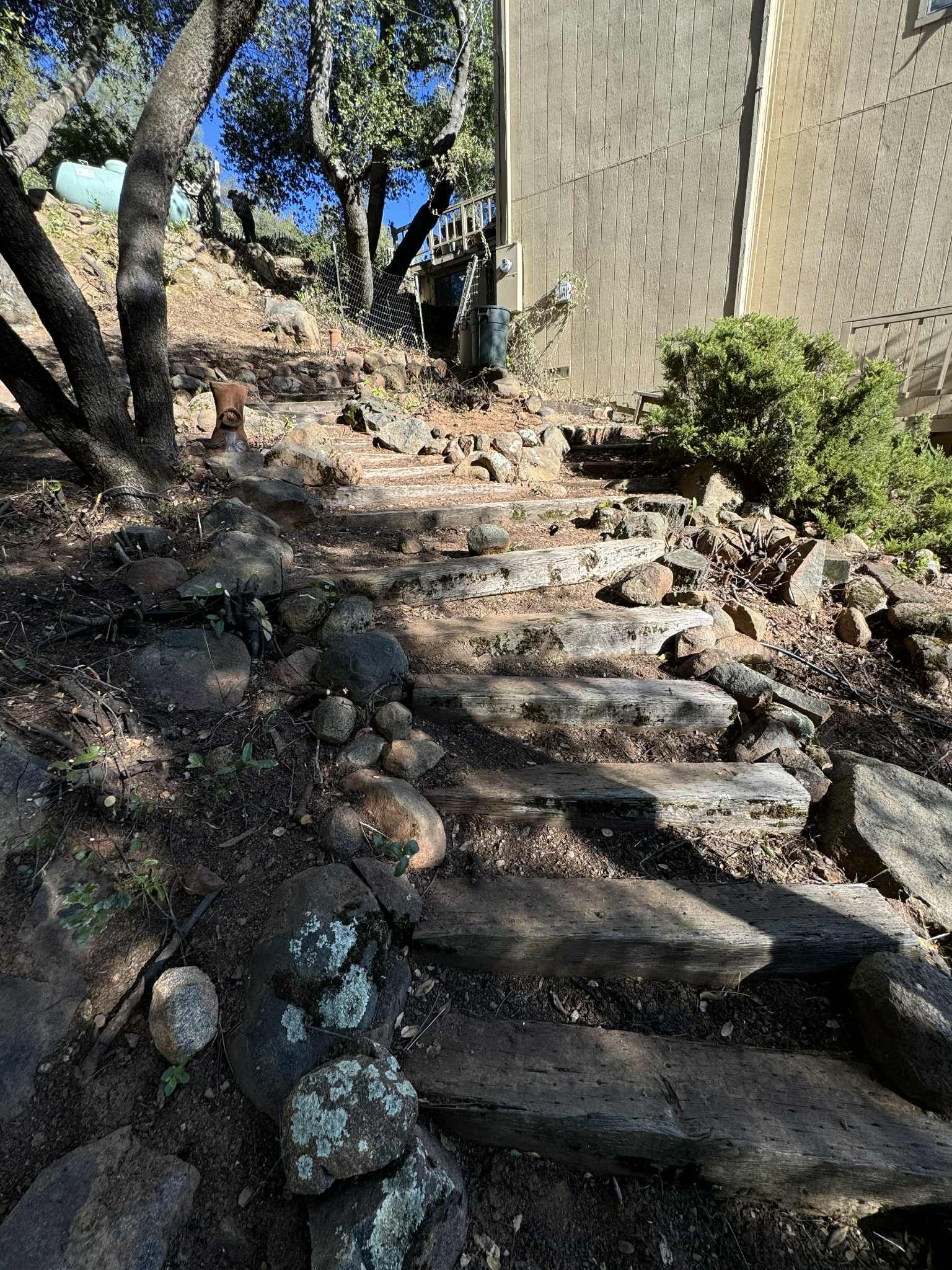 Stone steps leading uphill, alongside a building and trees; sunny outdoor setting.