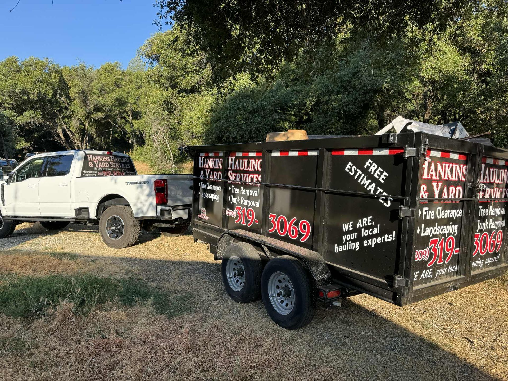 White pickup truck towing a black dumpster trailer with company logos; outdoors.