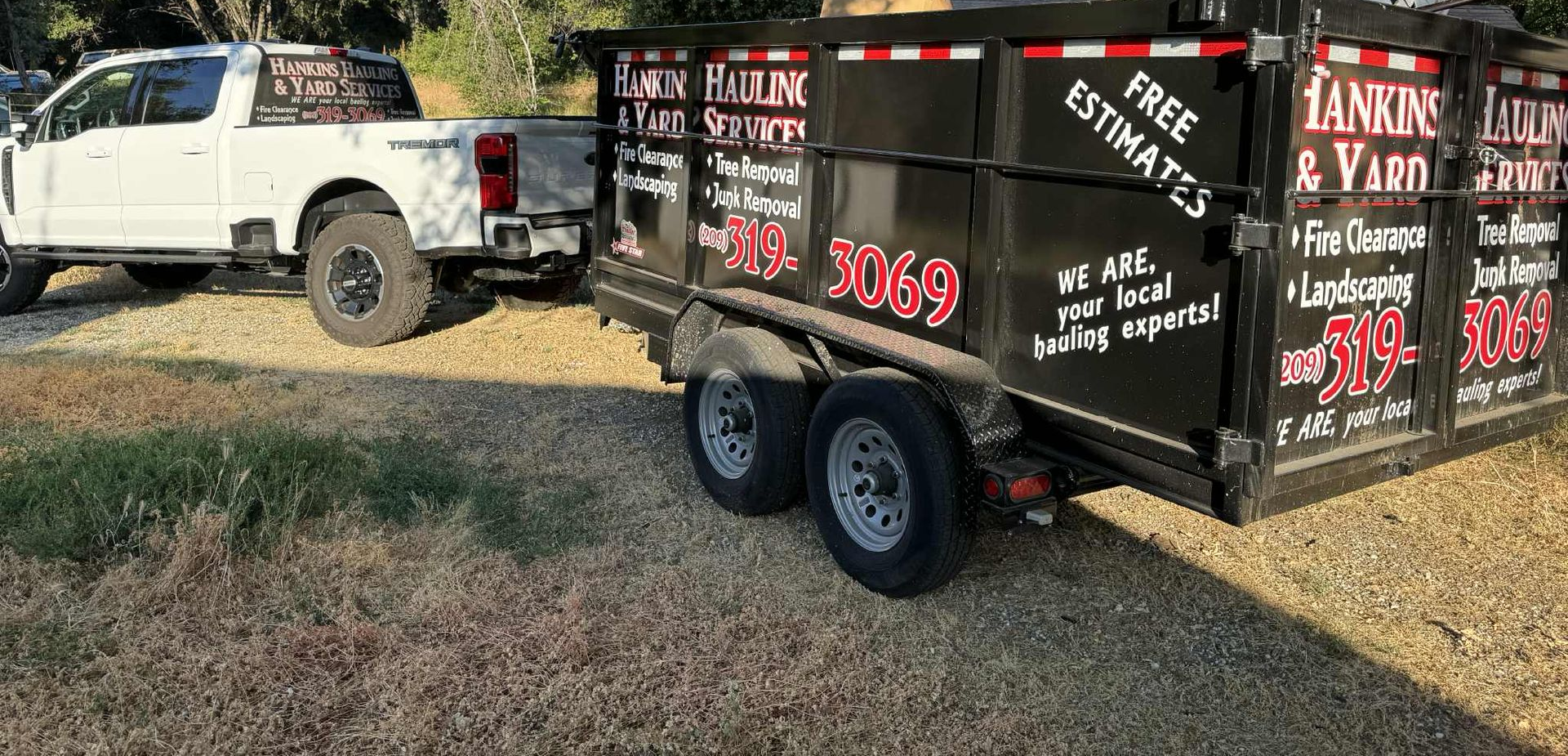 A white truck towing a black dumpster trailer with the business name 