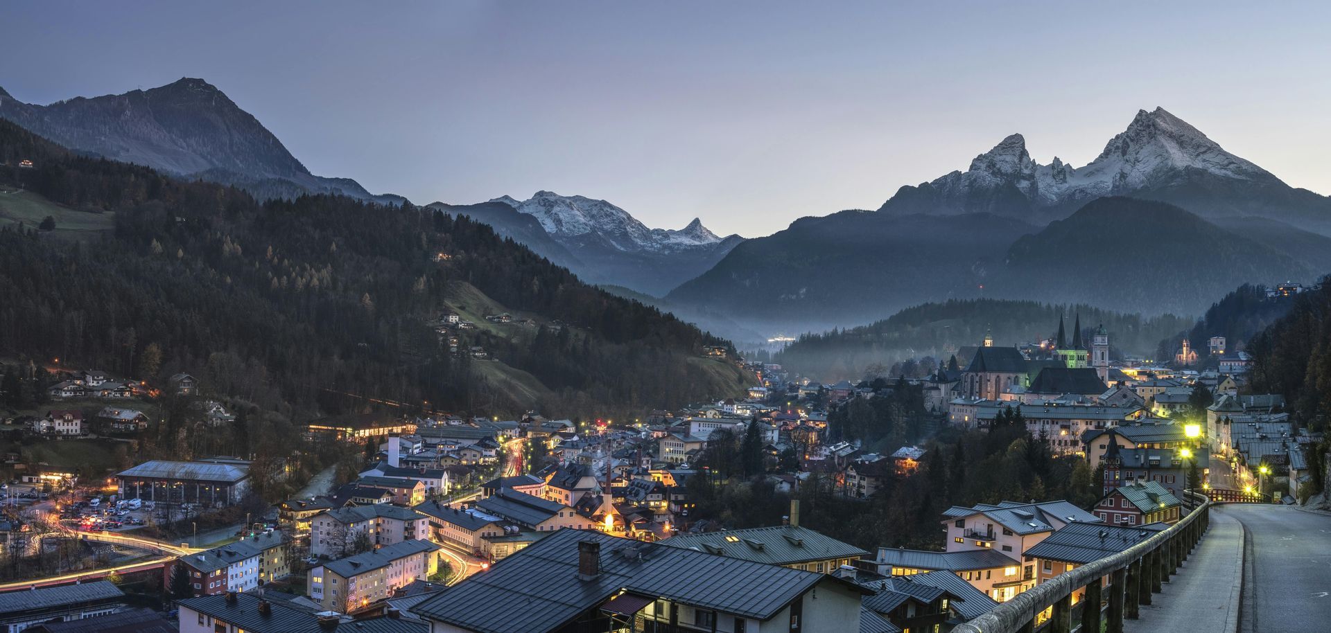 Nighttime view of a mountain town nestled in a valley, illuminated by streetlights, with mountains in the background.
