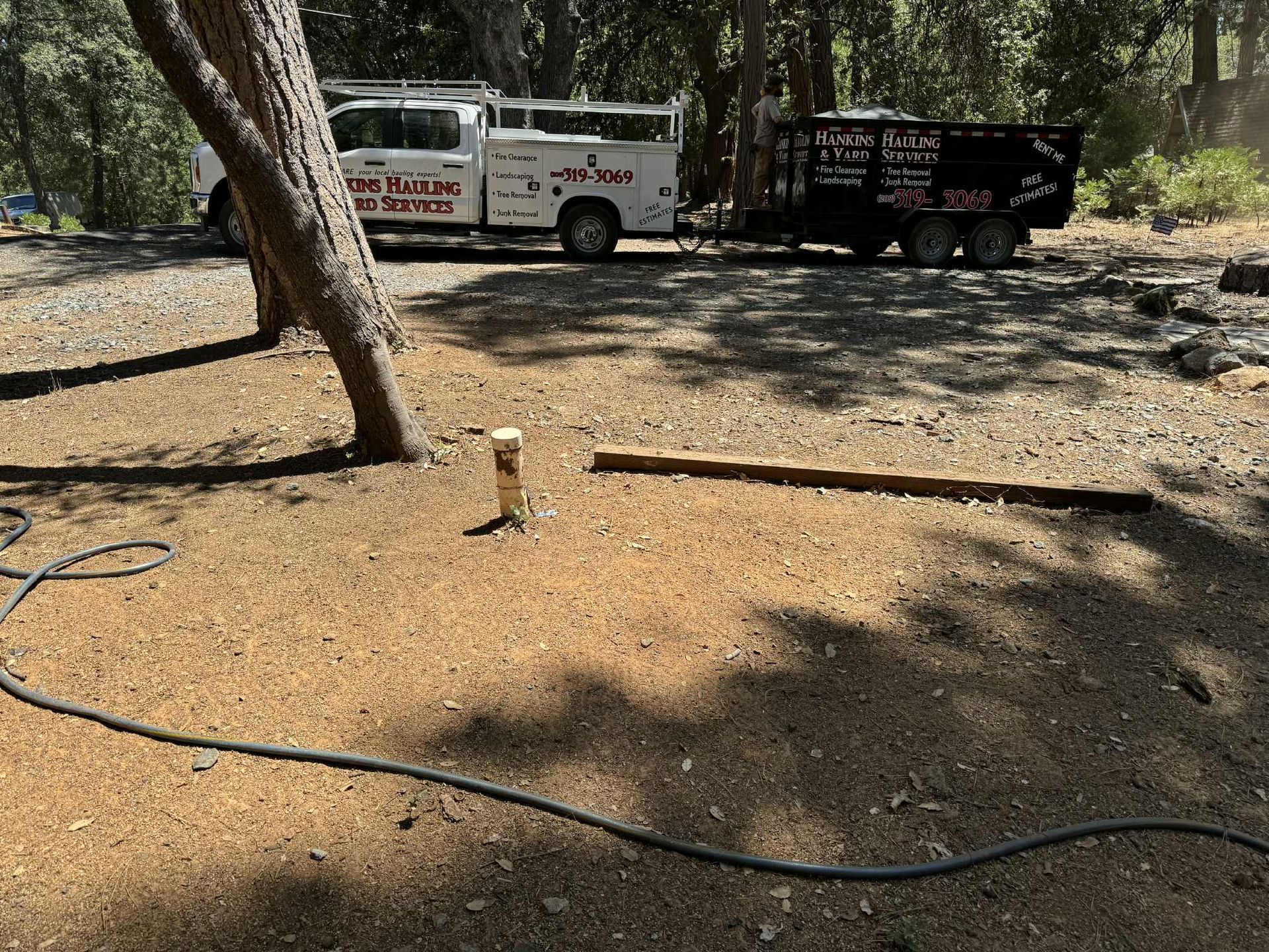 Truck and trailer parked on a dirt lot with a tree and a utility pipe visible.