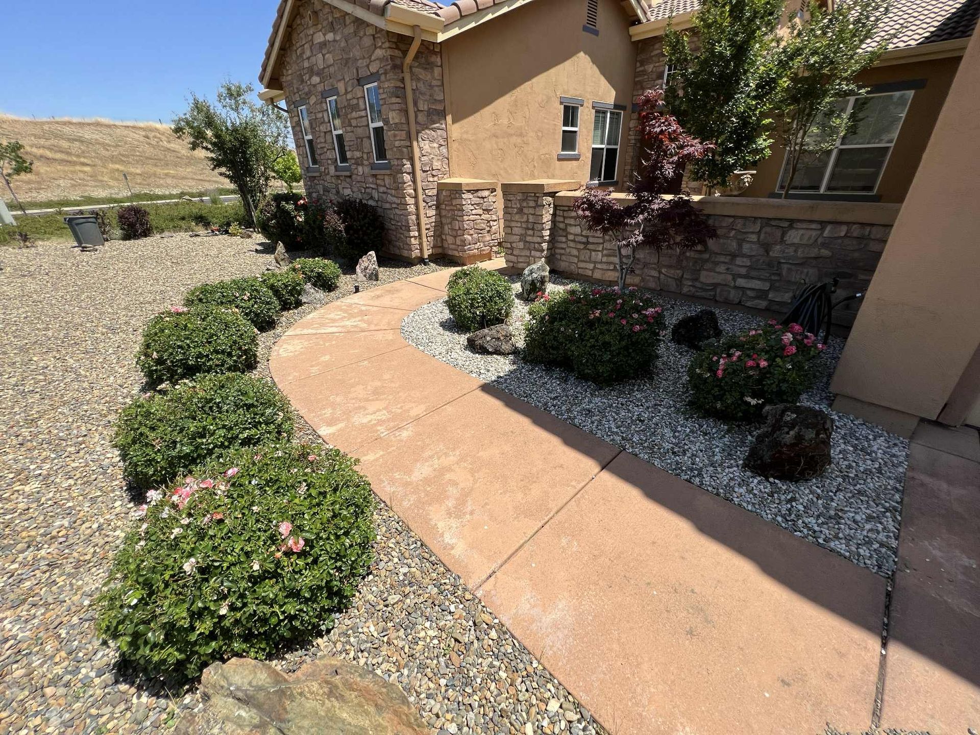 A stone-faced house with a curved walkway bordered by green bushes and gravel.