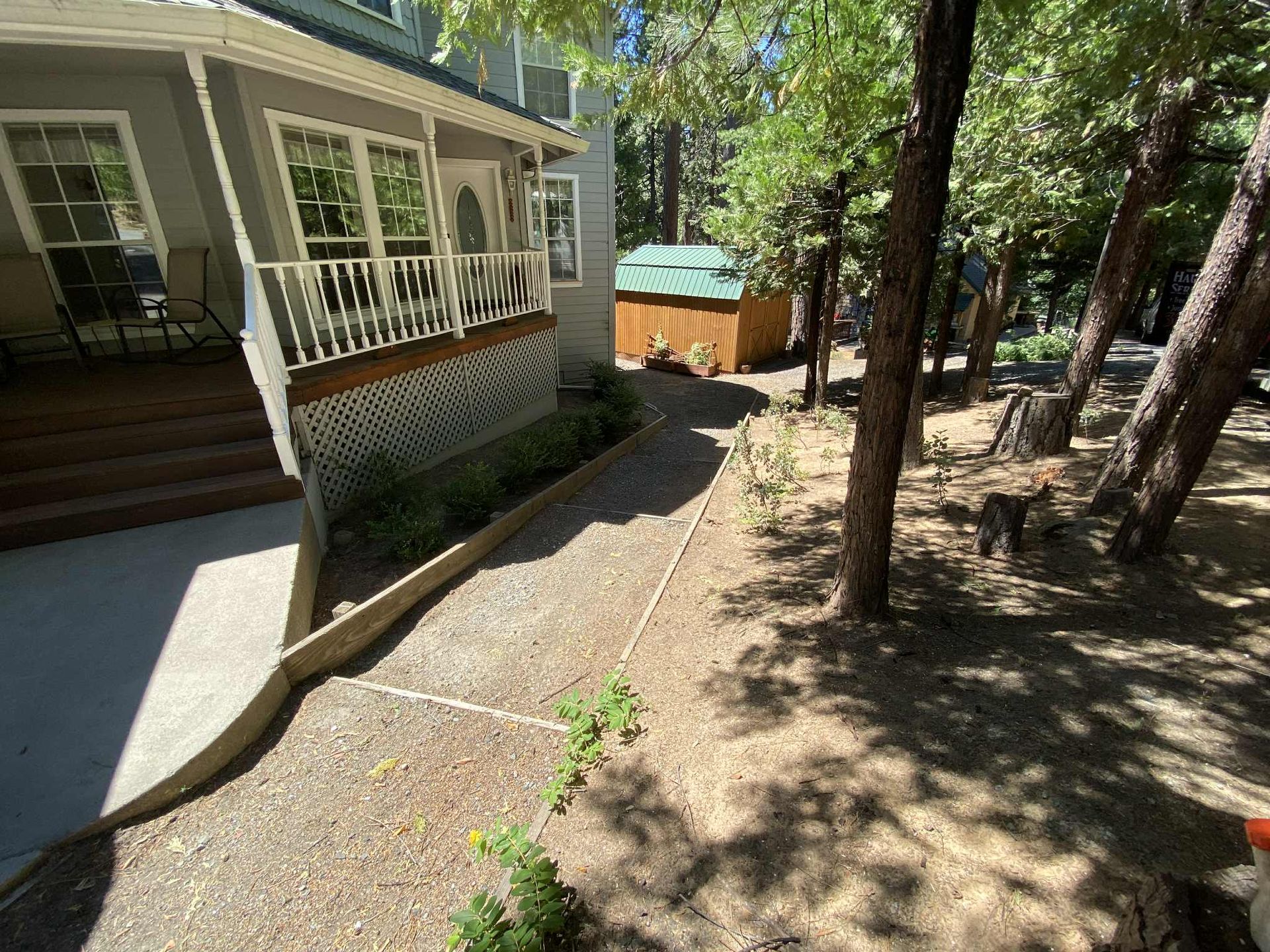 Exterior view of a house with a porch, gravel path, and trees in a sunny setting.