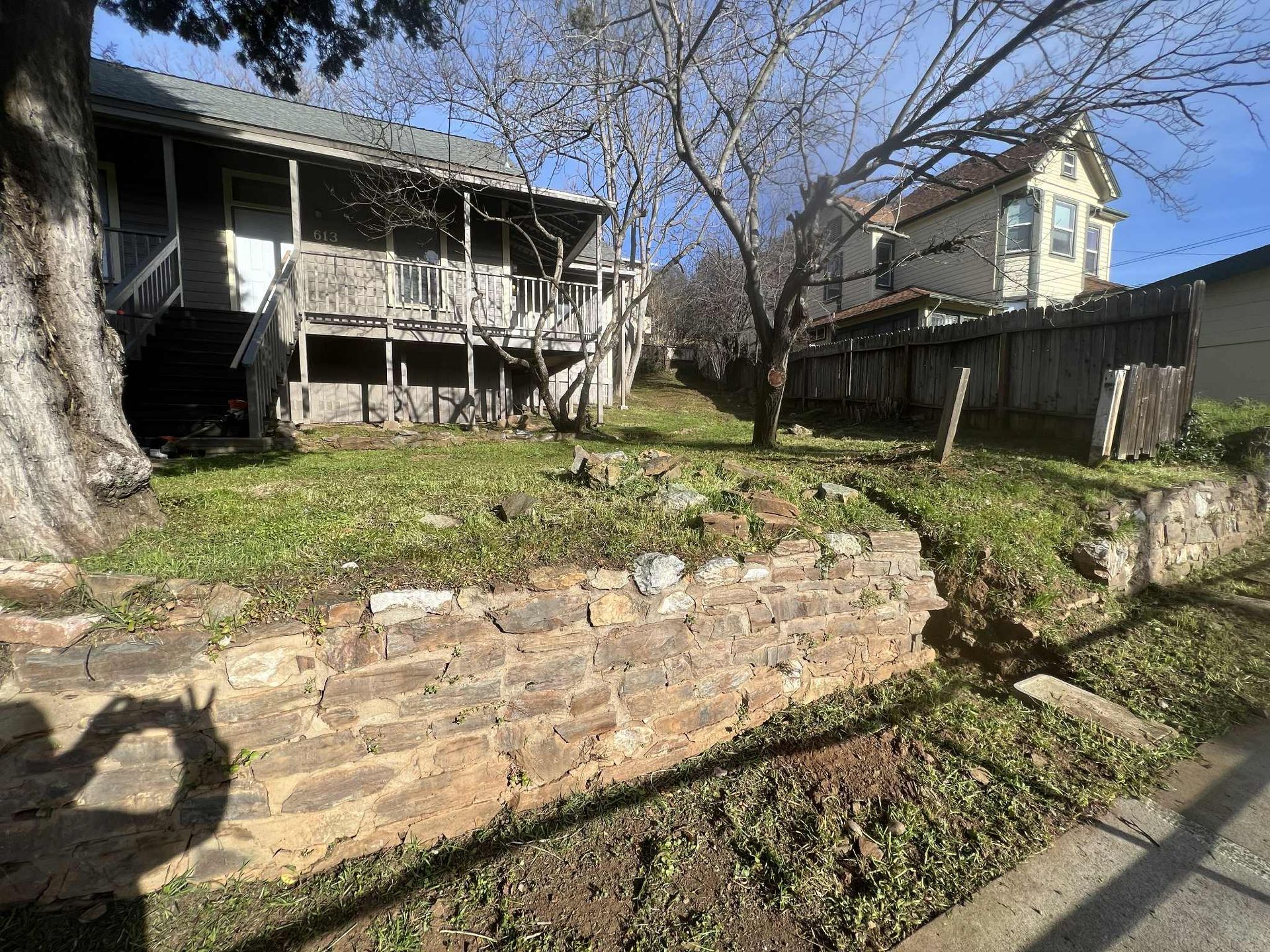 A small yard with stone retaining walls, with two houses in the background.