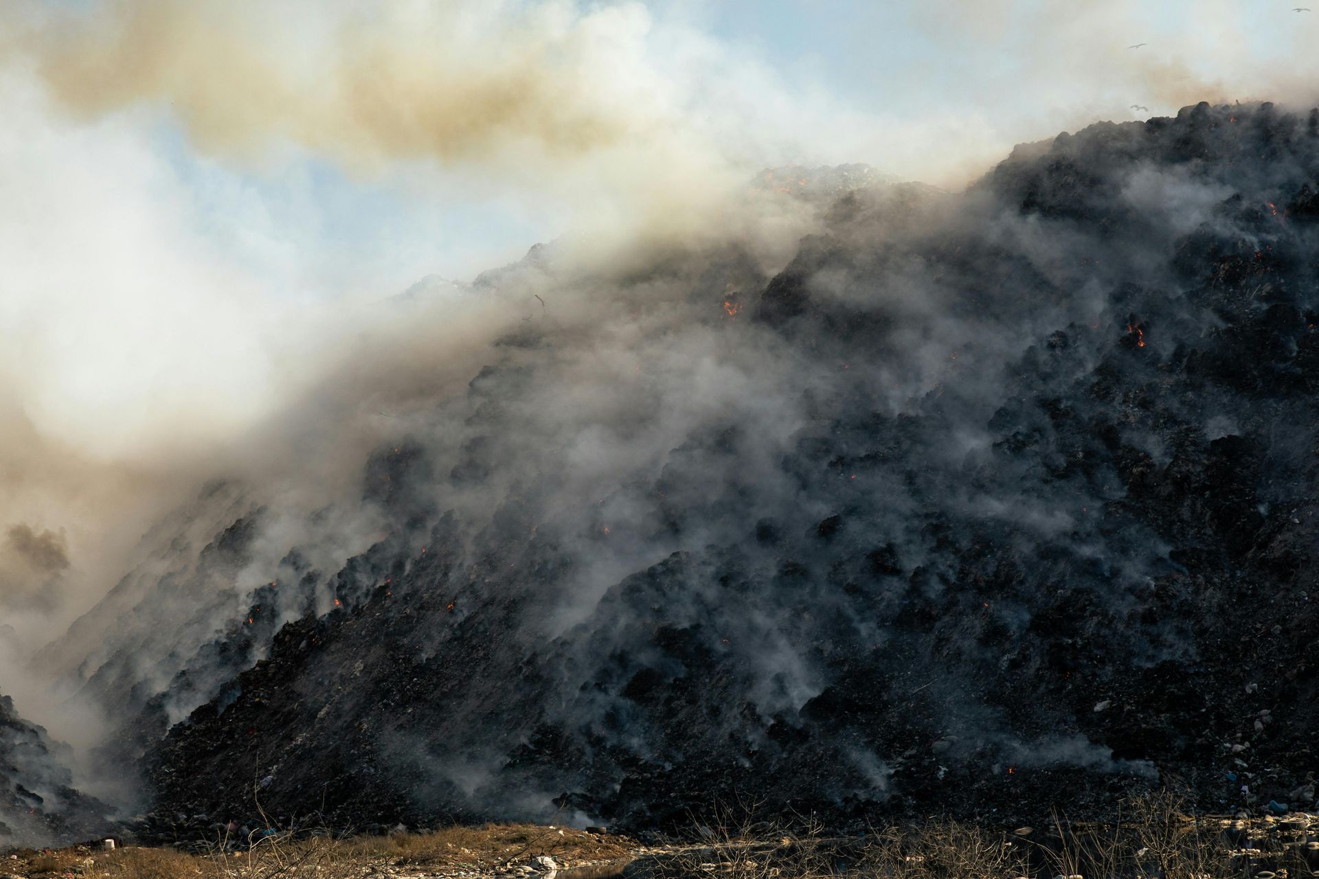 Dusty, smoky mountain of waste with smoke billowing into the sky.
