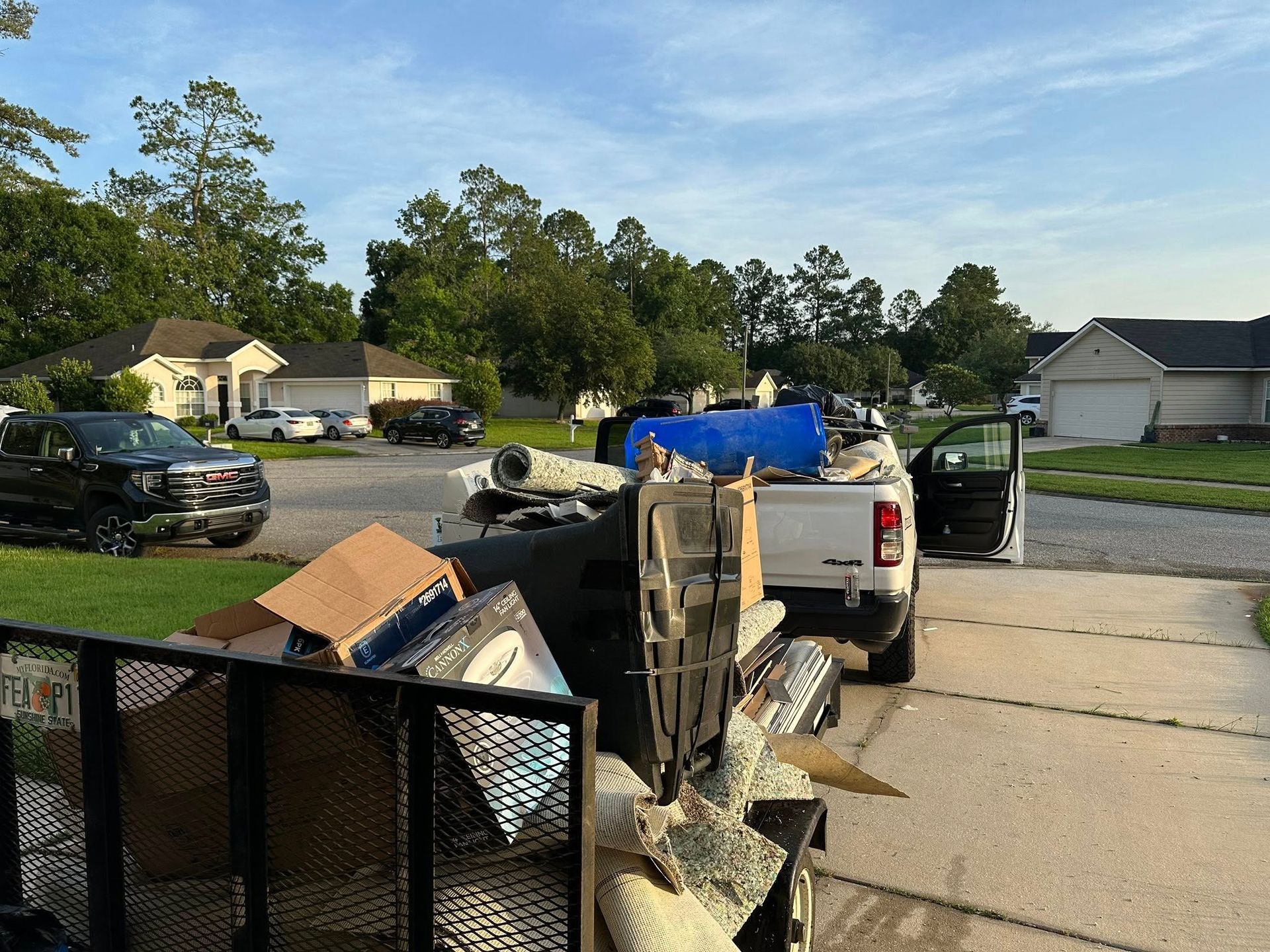 A truck and trailer loaded with debris parked in a residential driveway. Houses and trees are in the background.