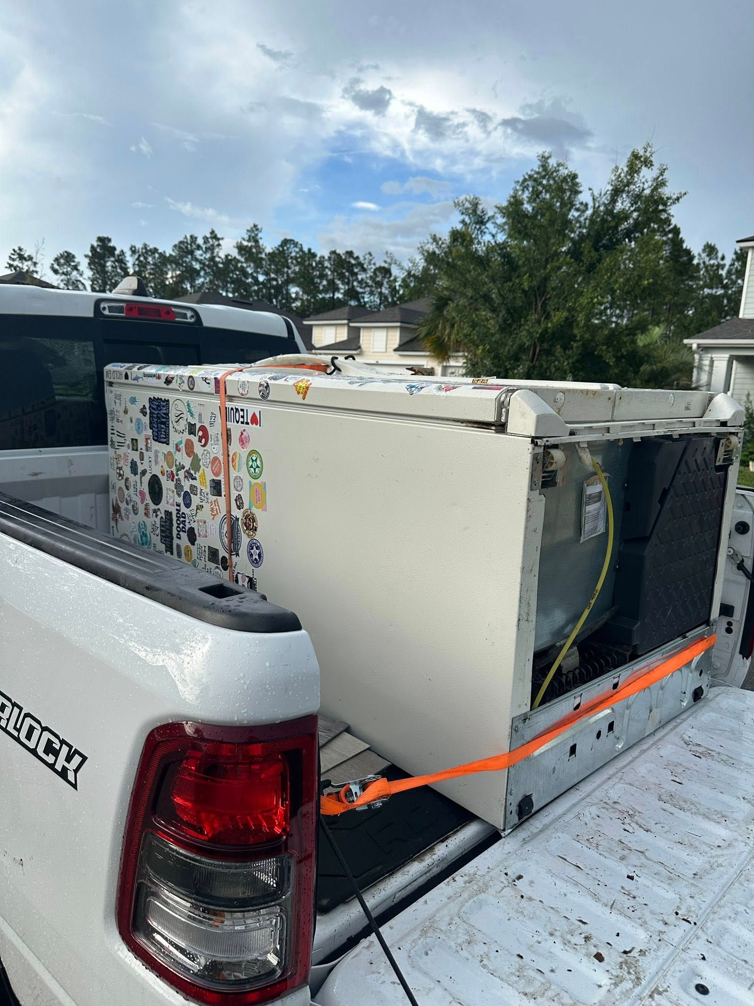 White truck bed carrying a large, white appliance secured with orange straps.