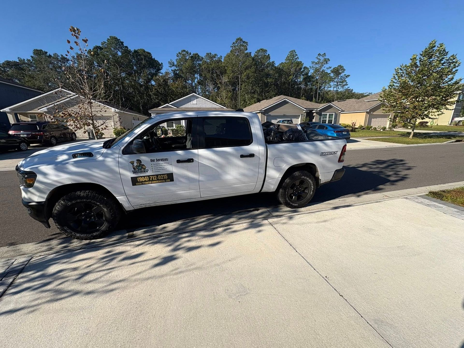 White pickup truck parked on a residential street; trees and houses in the background under a blue sky.