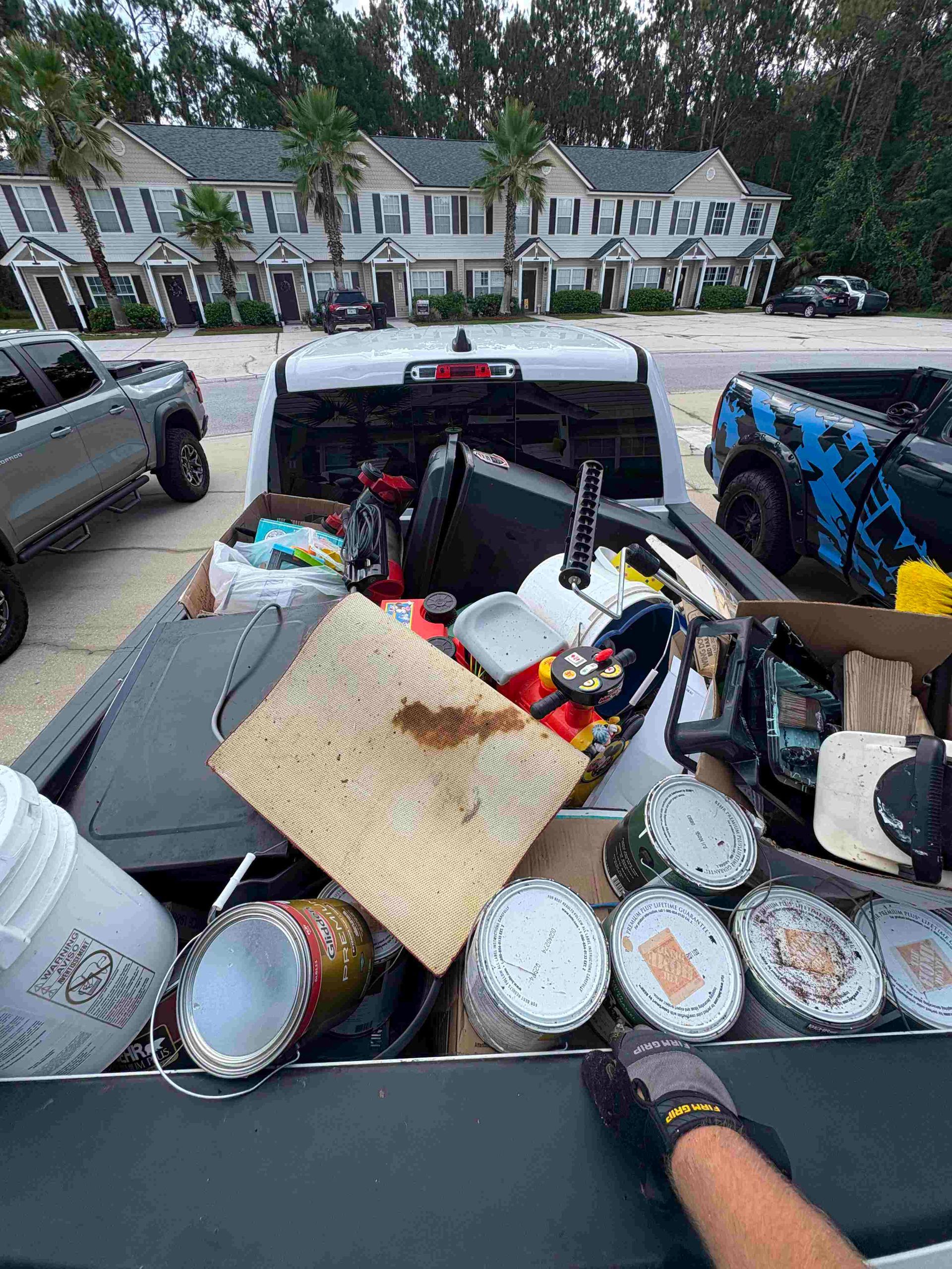 A truck bed overflowing with trash, paint cans, and debris, parked in front of townhouses.