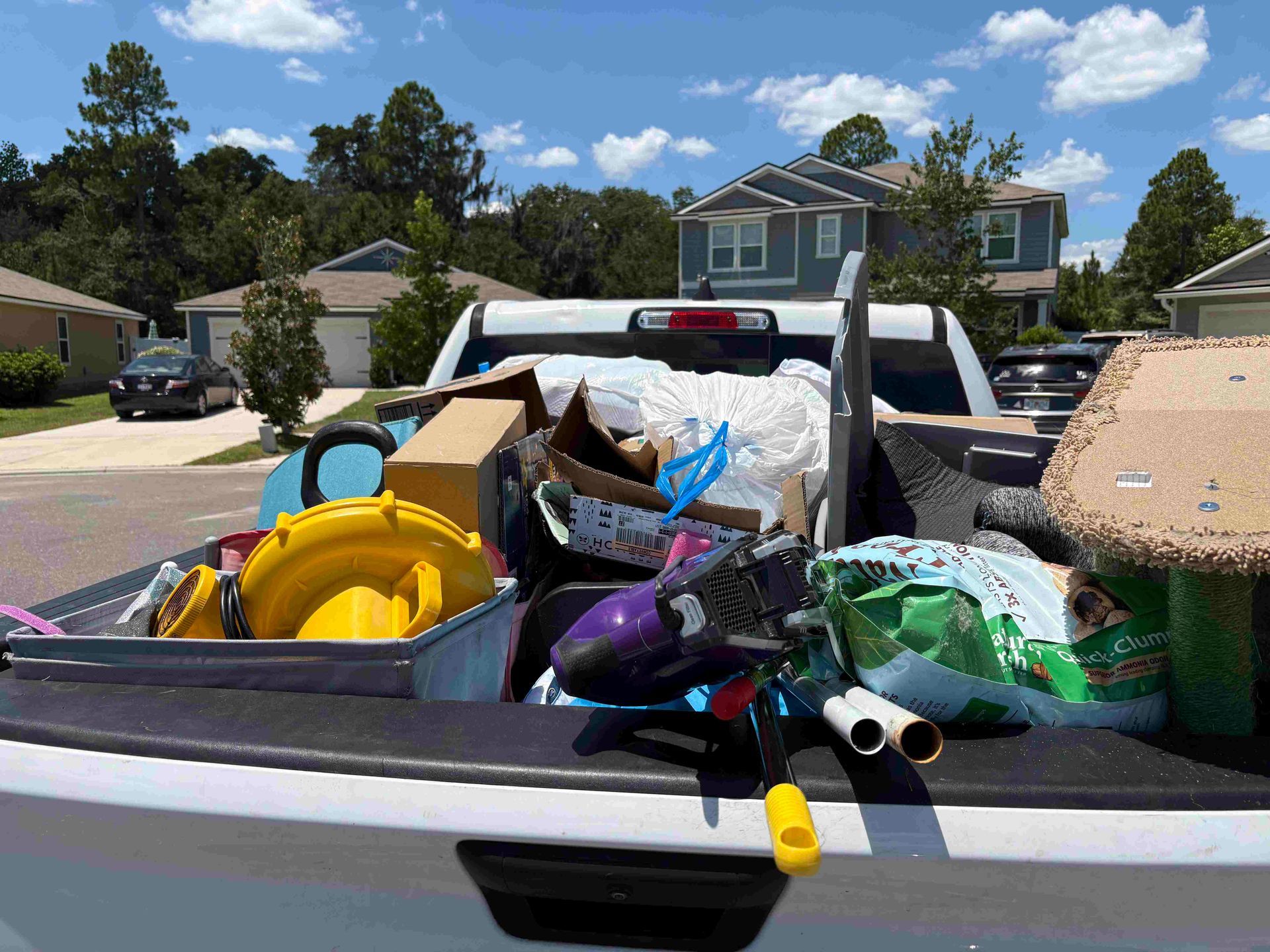 Pickup truck bed filled with trash and items; residential neighborhood backdrop.