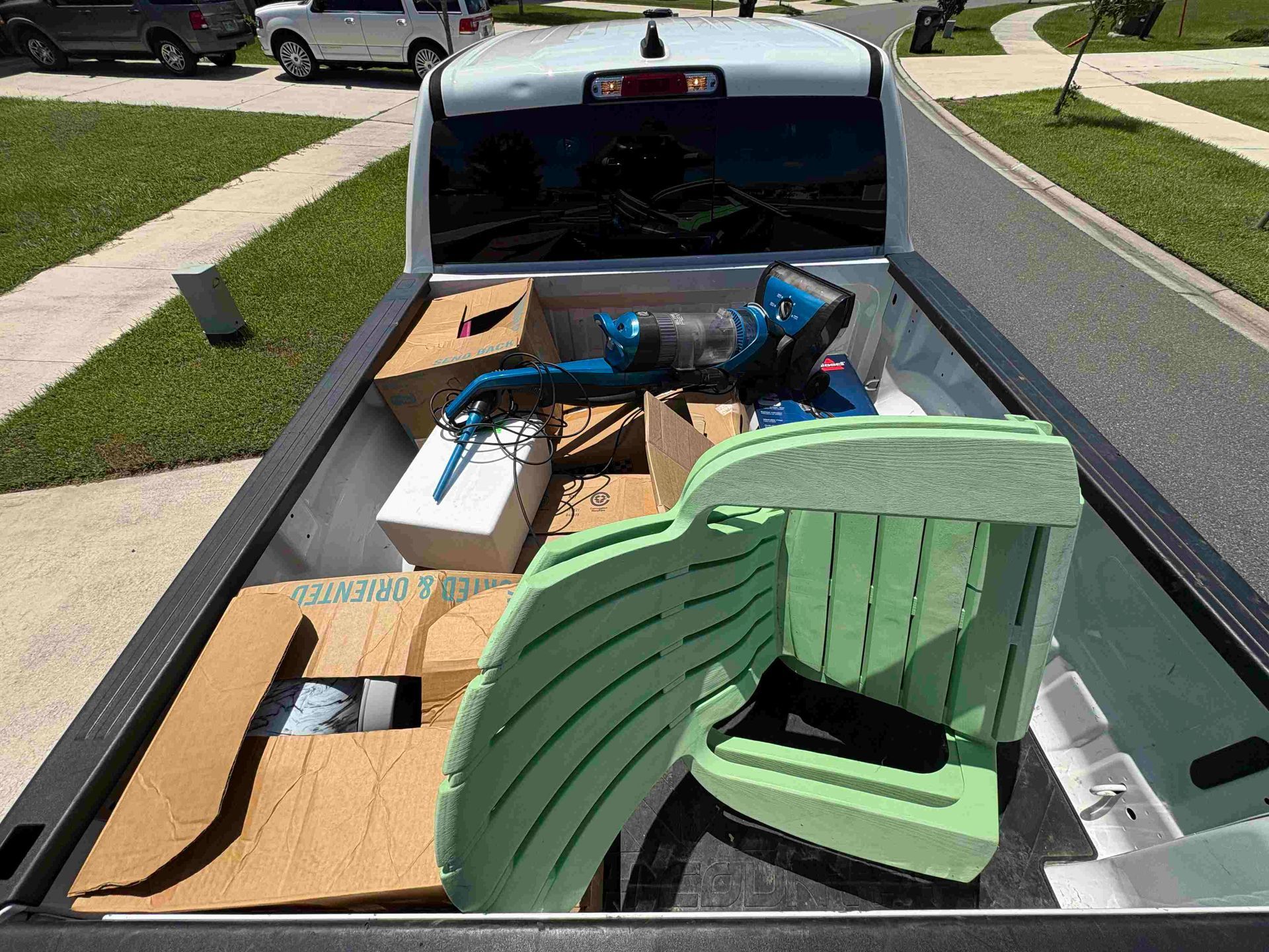 Truck bed filled with cardboard boxes and a green foam chair.