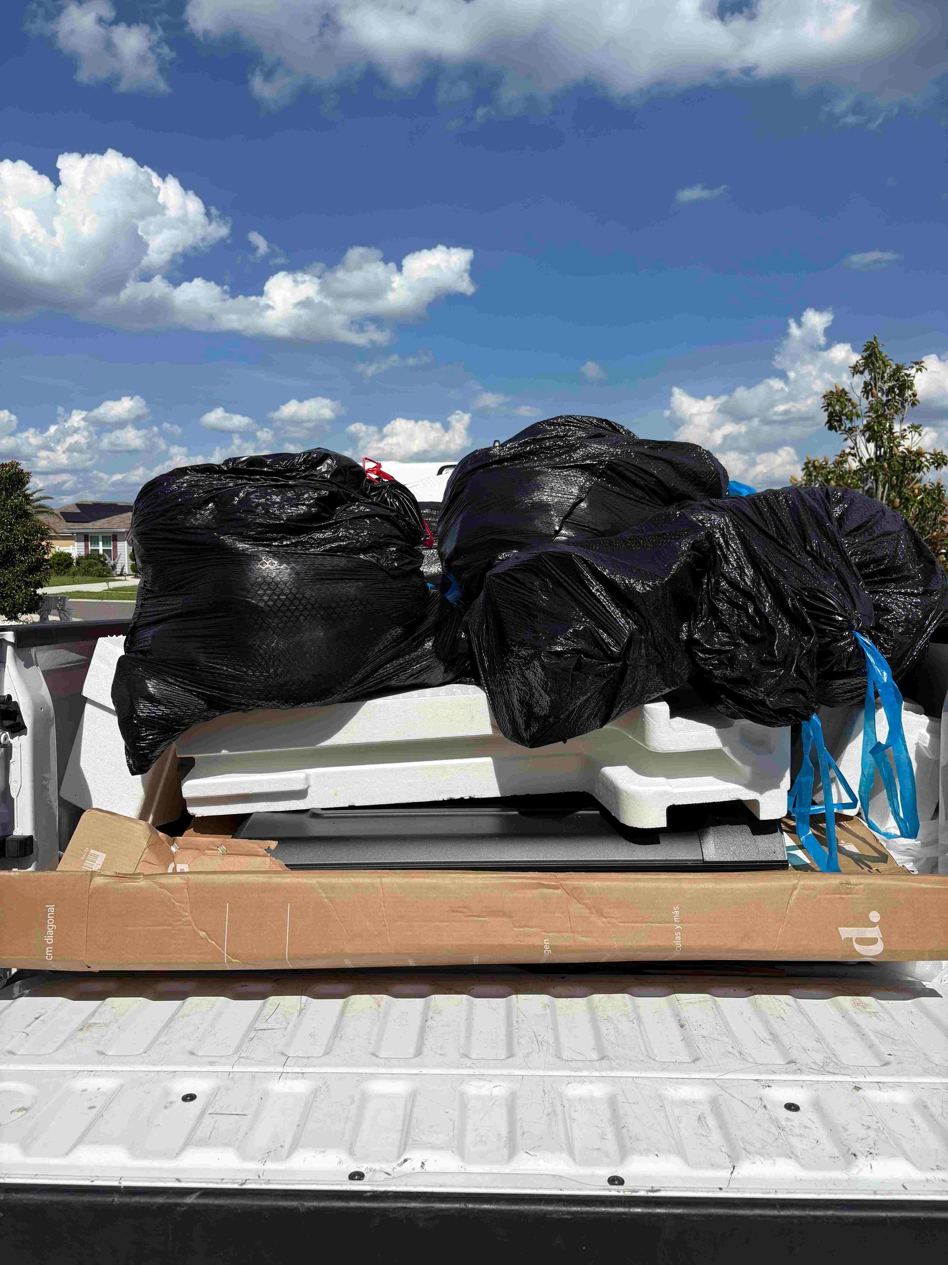 Truck bed loaded with black trash bags and white plastic containers under a cloudy sky.