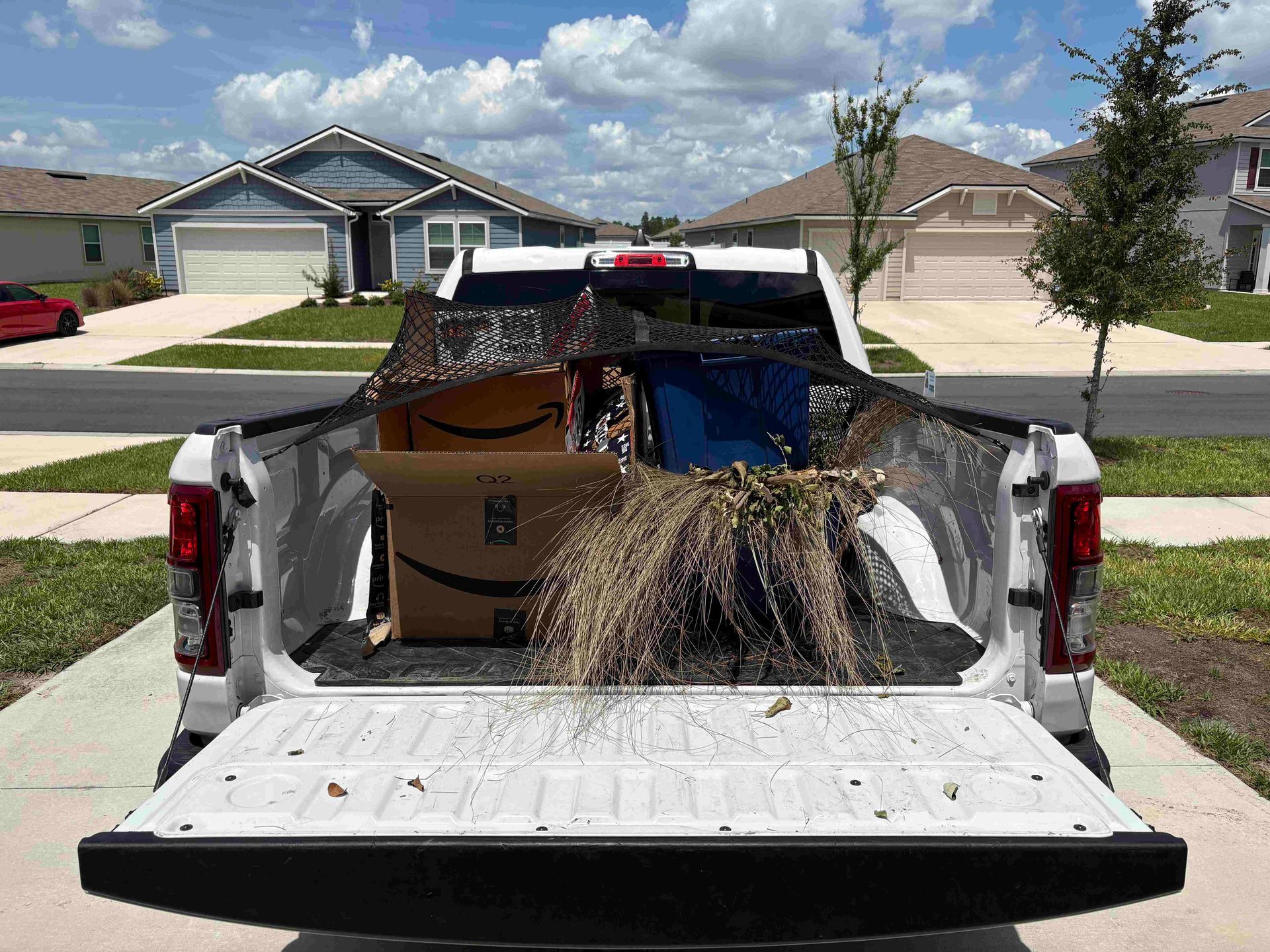 White pickup truck bed filled with boxes and debris, secured by a cargo net, parked in a driveway.