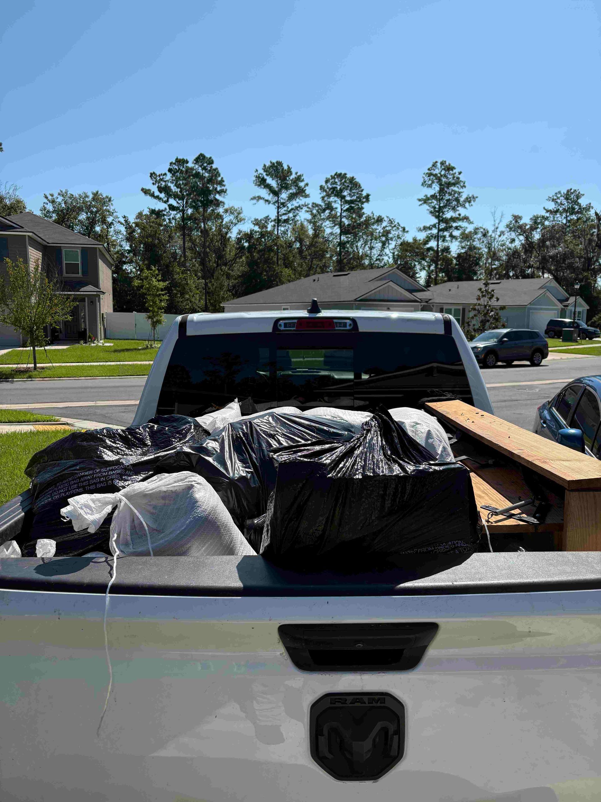 Pickup truck bed loaded with trash bags, boards, and other debris. Sunny day in a residential area.