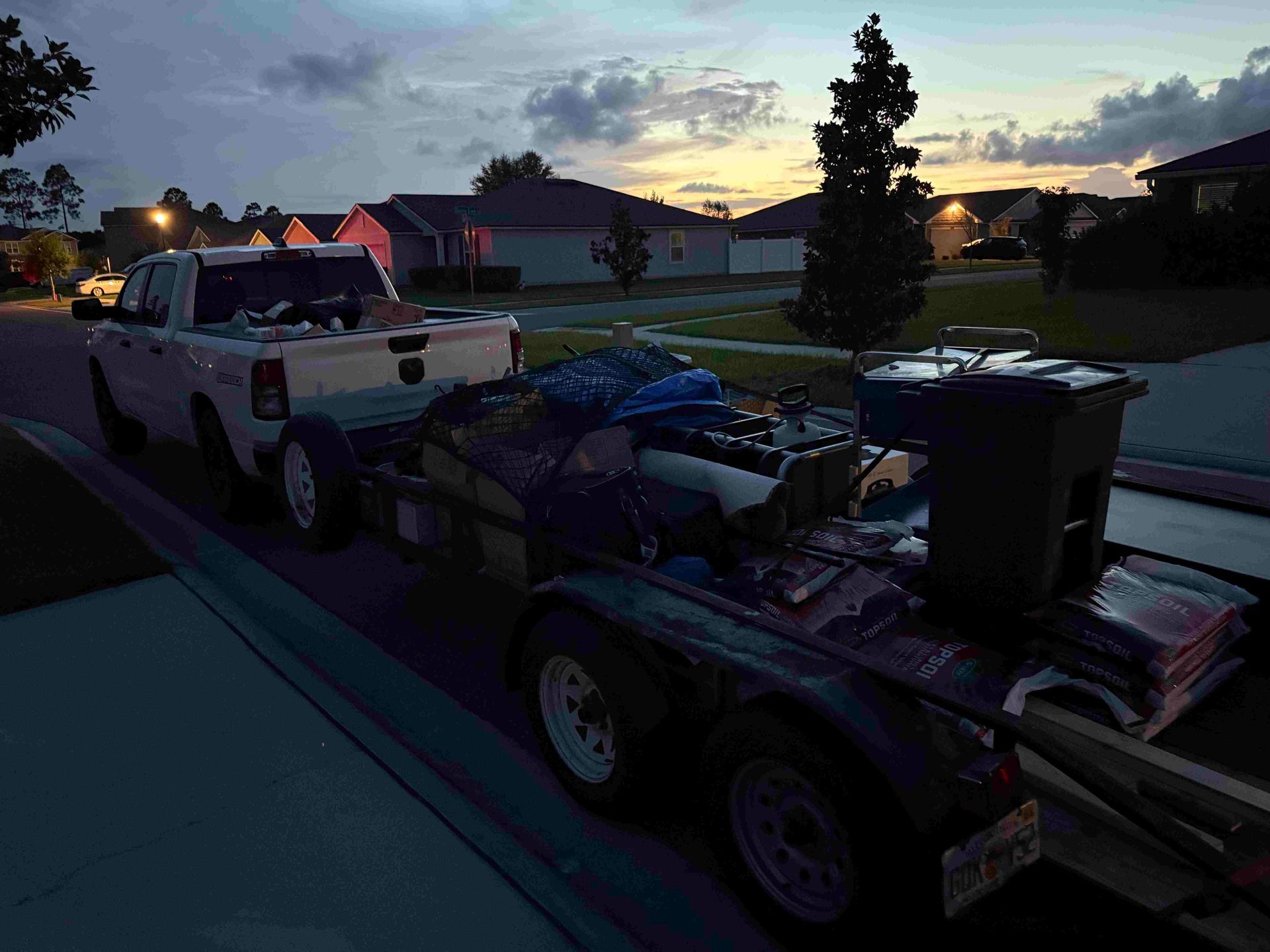 Truck pulling a trailer loaded with items, parked on a residential street at dusk.
