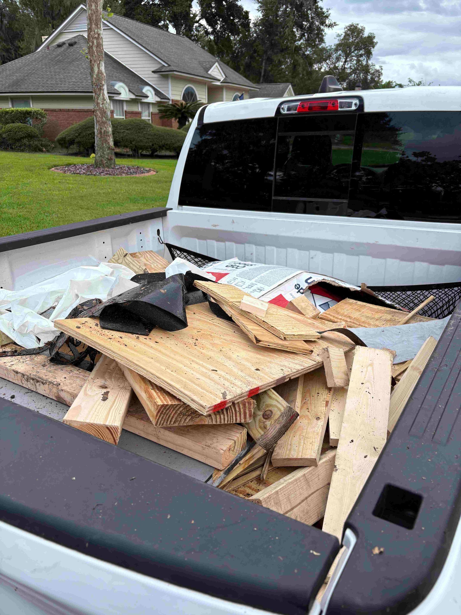 White pickup truck bed filled with construction debris, parked in front of a house.