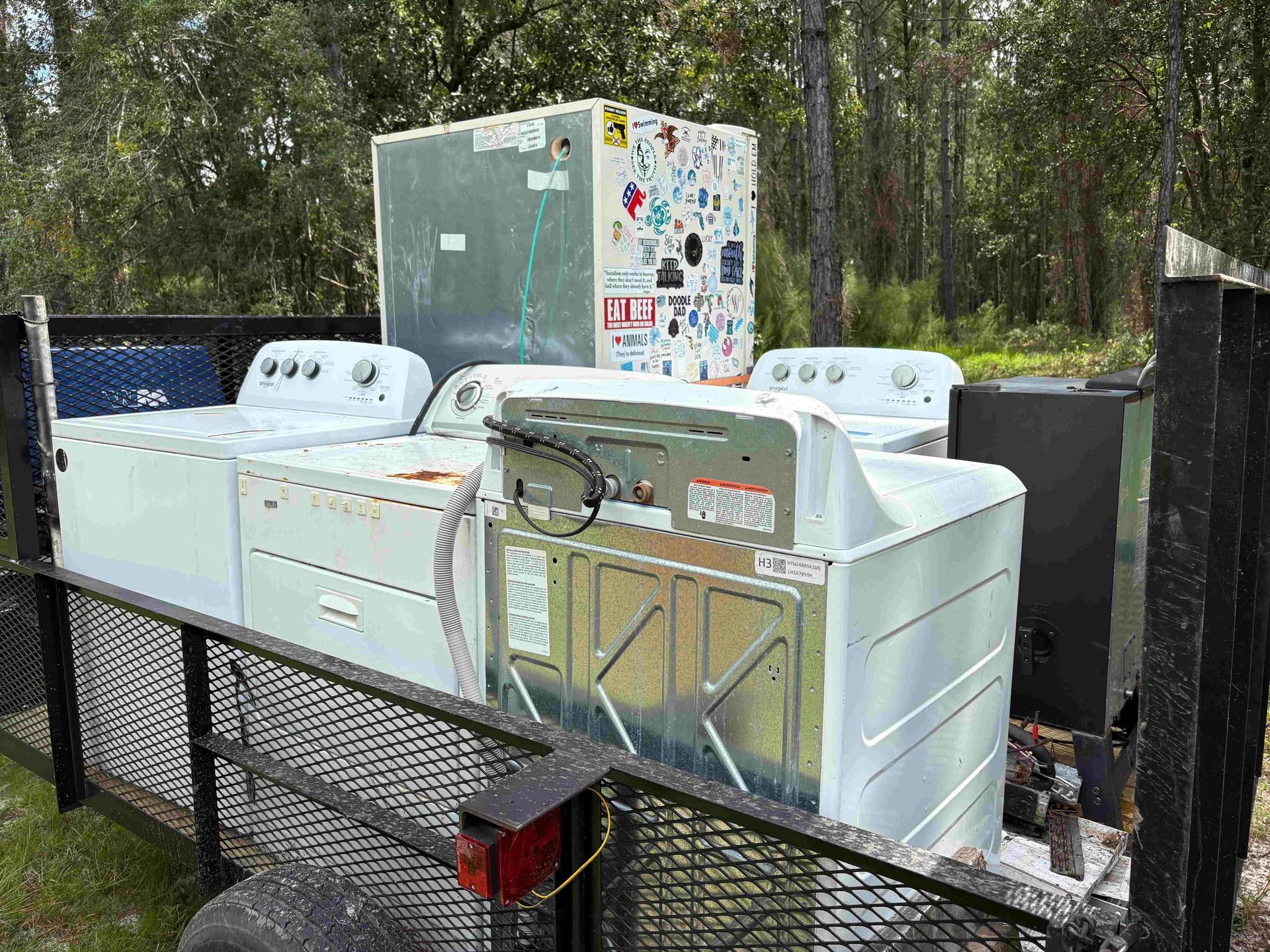 Appliances on a trailer: washing machines, dryer, and refrigerator ready for disposal, outdoors.