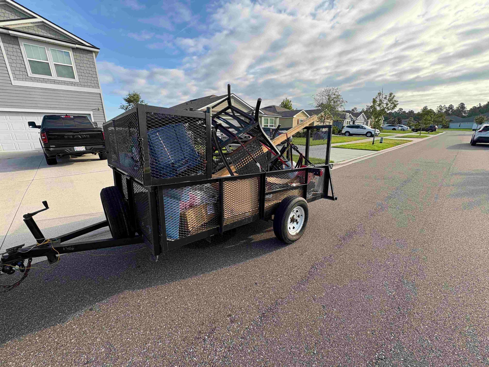 A trailer filled with debris parked on a residential street. A black truck is in the background.