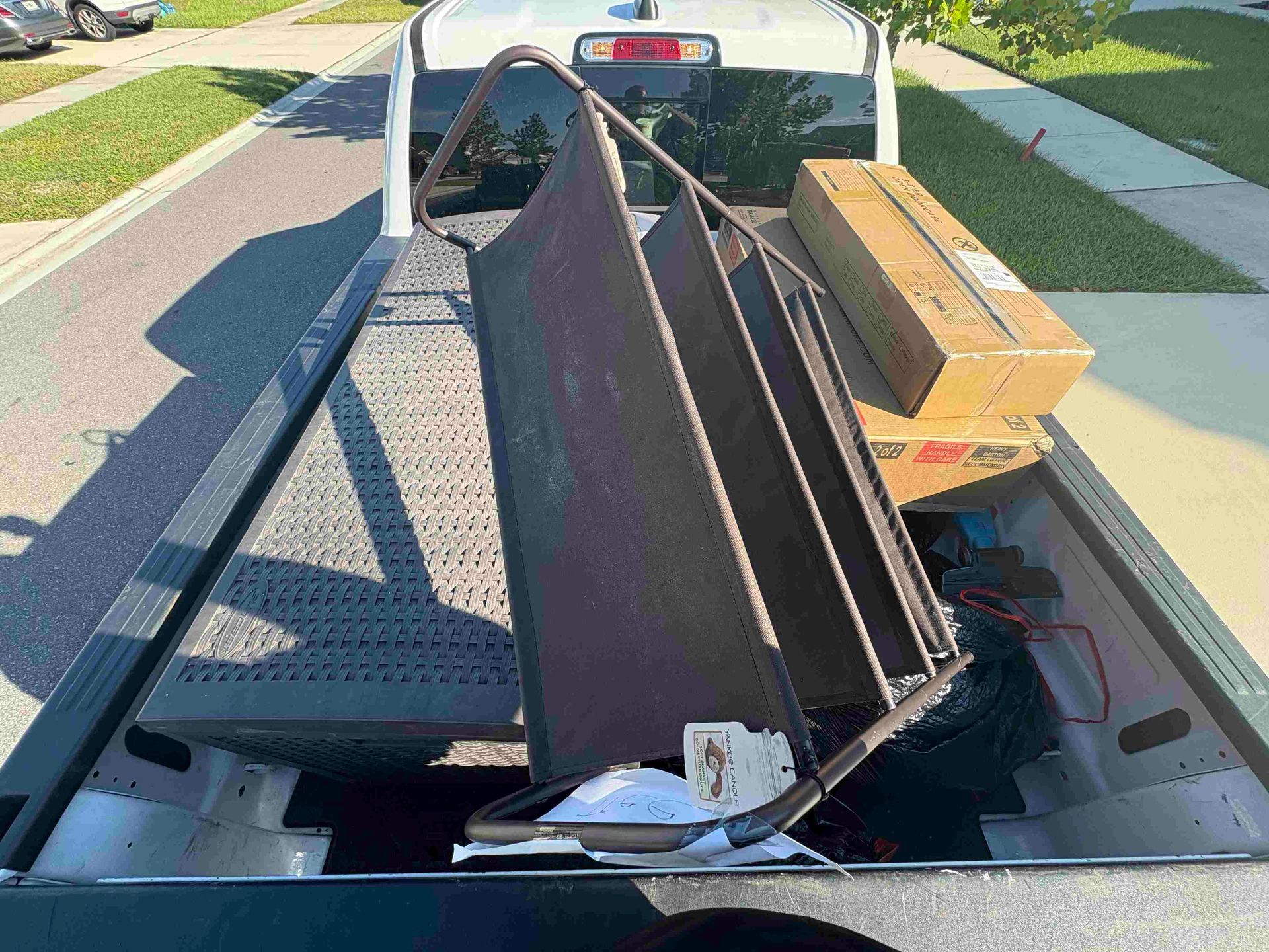 A truck bed loaded with metal frame, boxes, and debris. Outdoors on a sunny day.