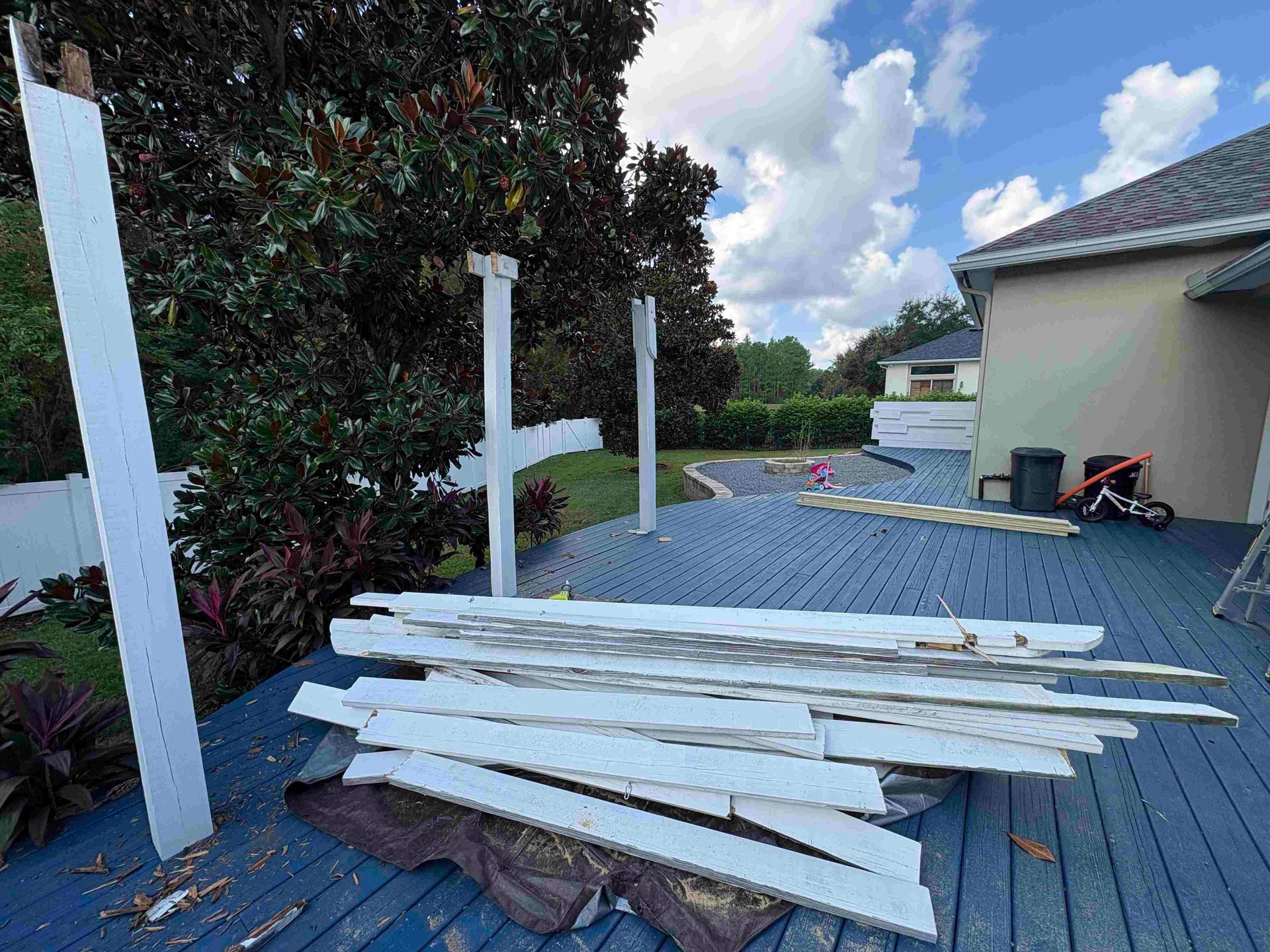 Deck being dismantled; white posts and planks scattered on blue-painted wood.  Backyard setting, partially cloudy sky.