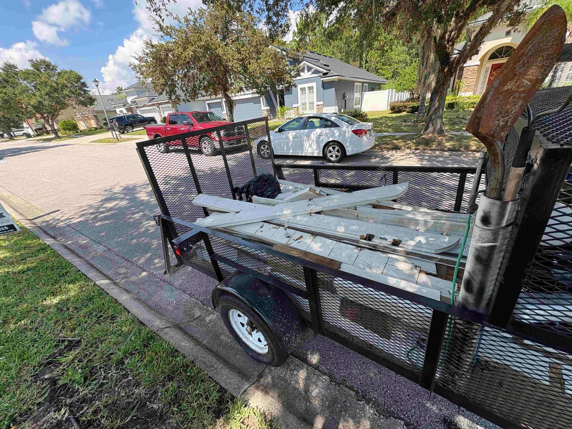 Trailer loaded with debris parked on a residential street. White and gray buildings in the background.