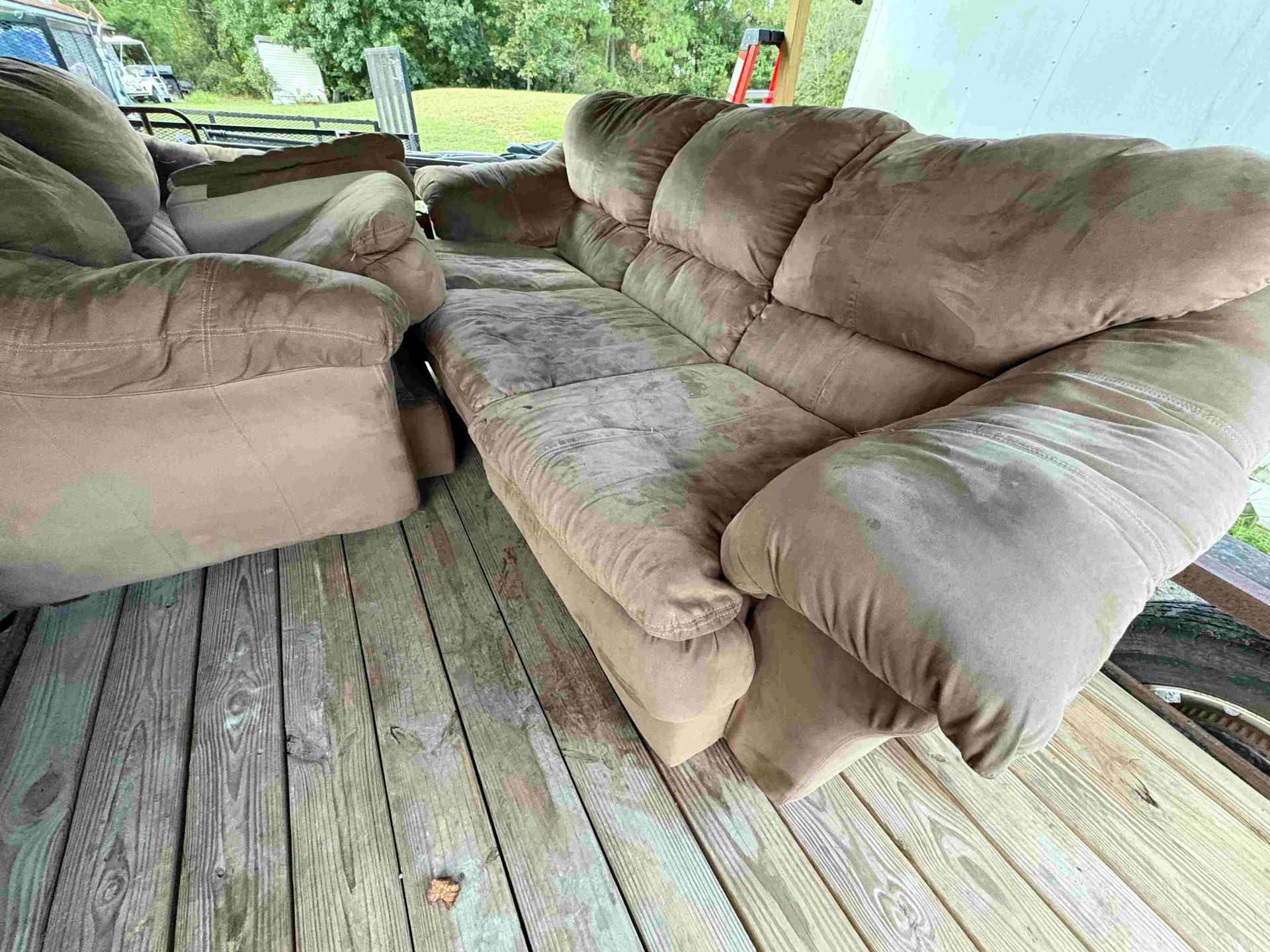 Brown, worn couch and recliner on a weathered wooden deck.