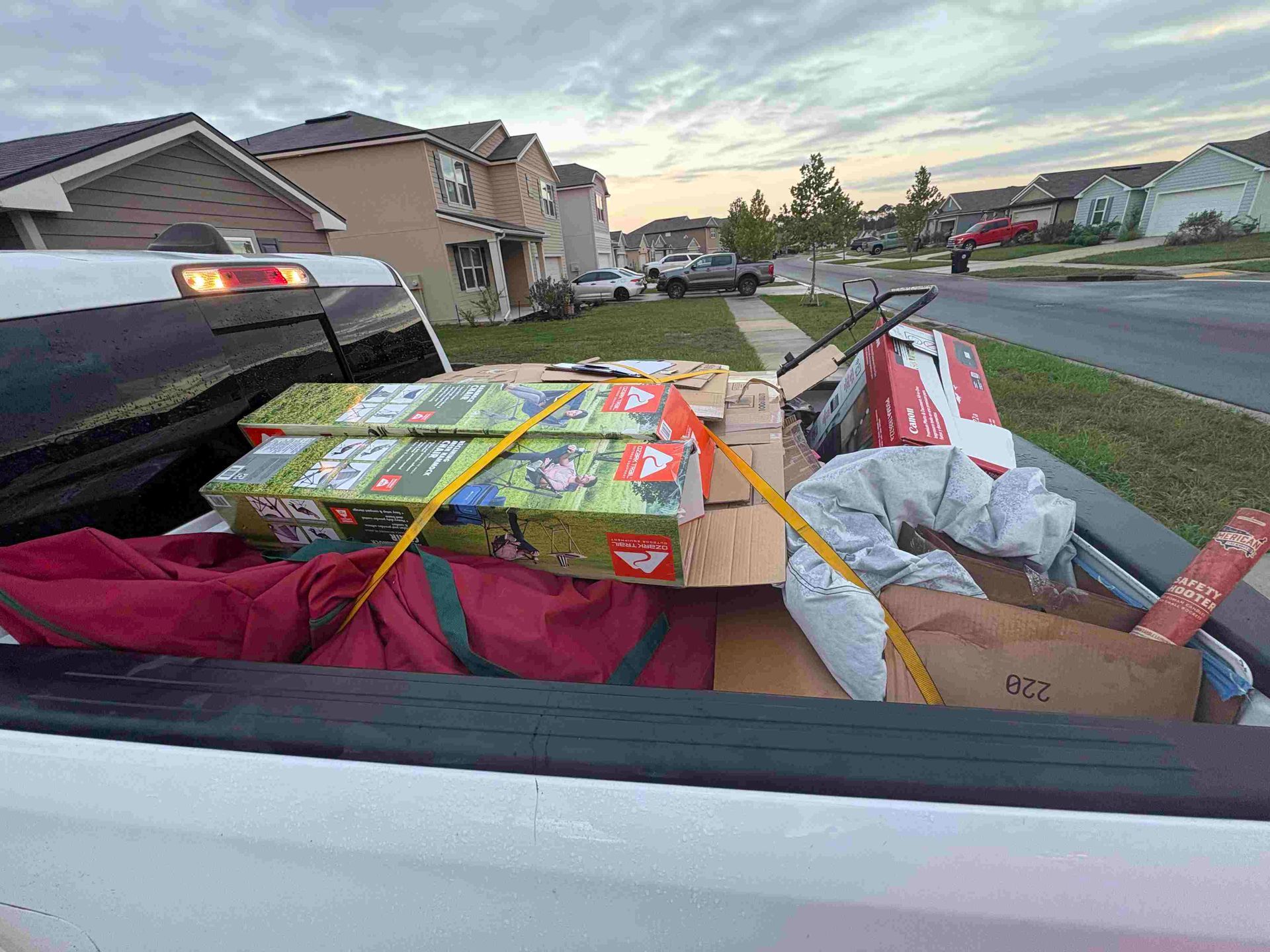 Truck bed loaded with boxes and items, secured with straps, in a suburban neighborhood.