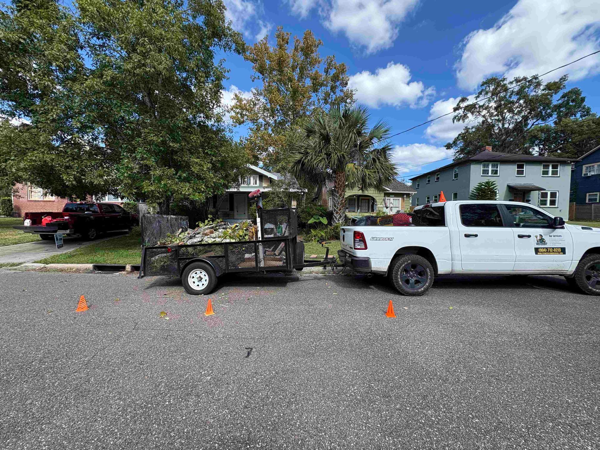 White pickup truck with trailer containing yard waste parked on a street near homes.