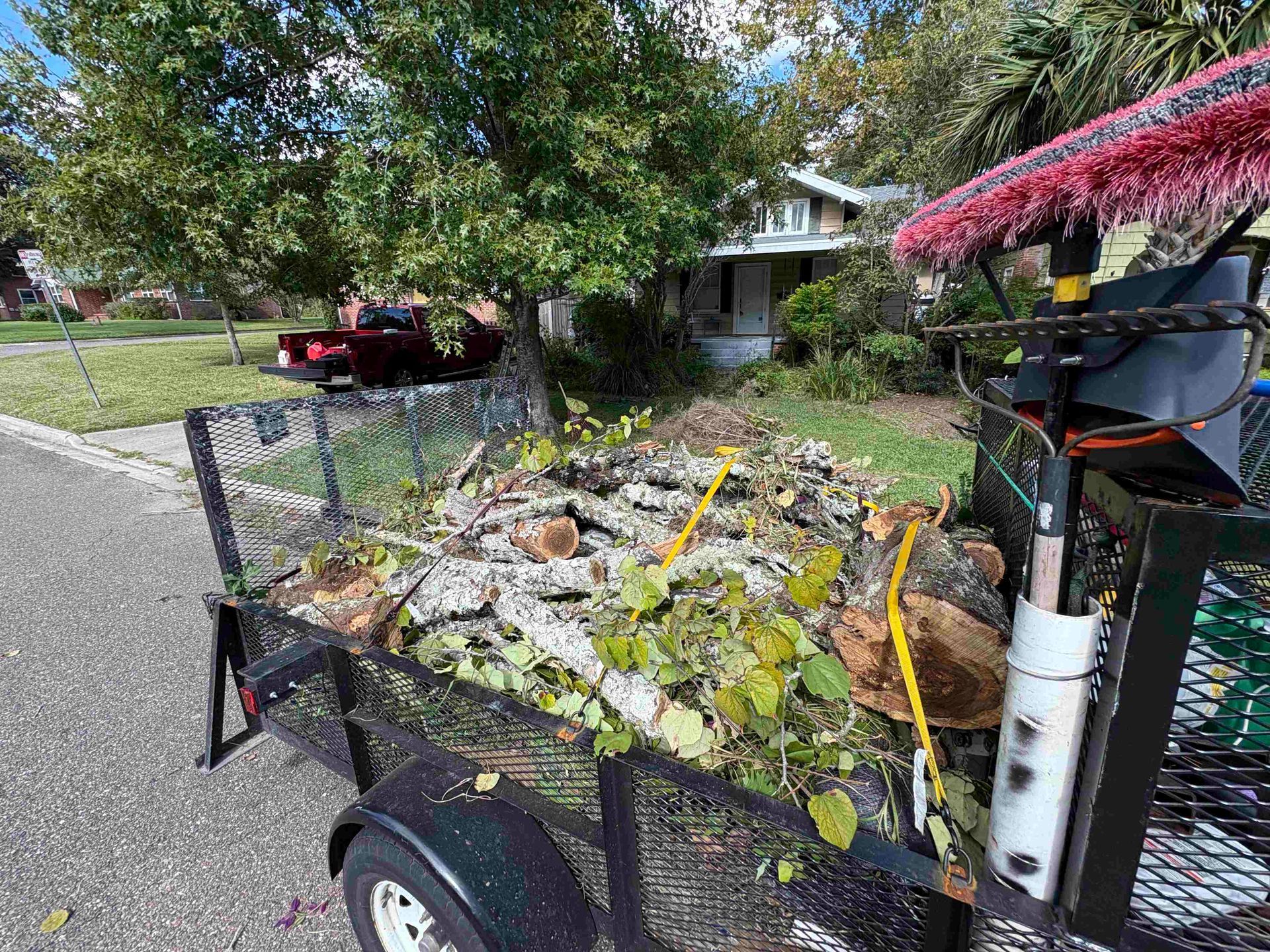 Trailer filled with tree branches and yard waste on a residential street. A house is in the background.
