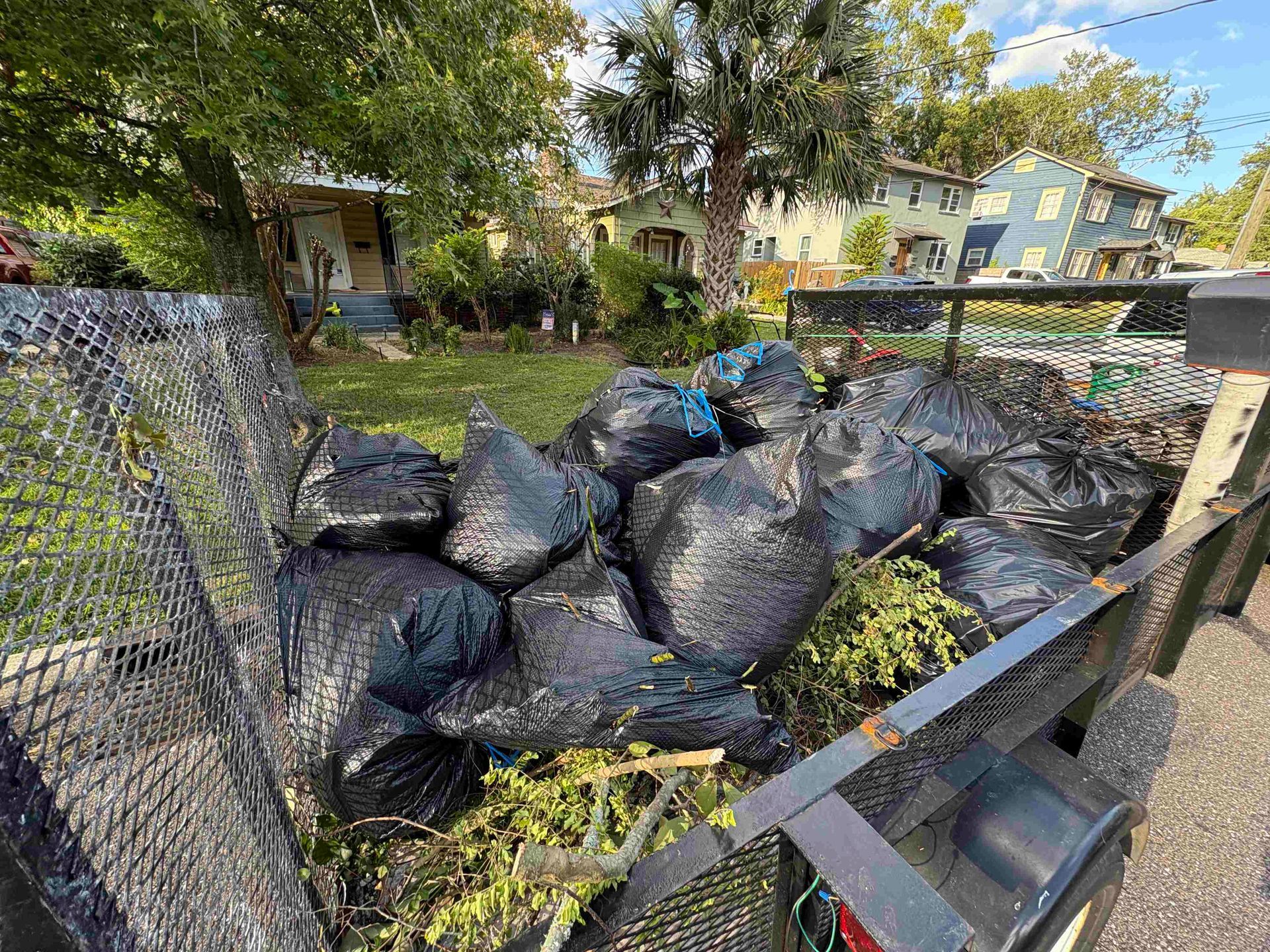 A trailer loaded with several black trash bags filled with yard waste, in a residential area.