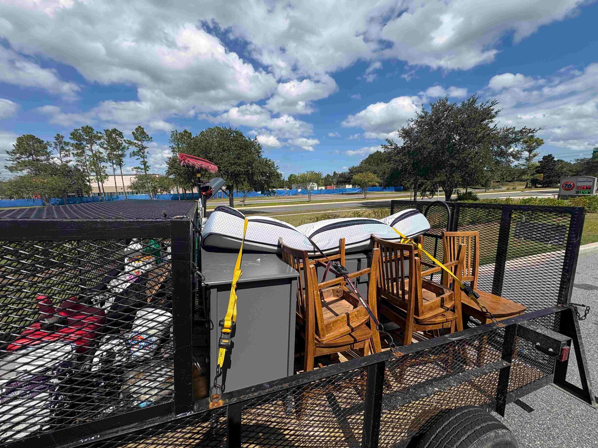 Trailer loaded with furniture and cushions, secured with yellow straps, on a sunny day.
