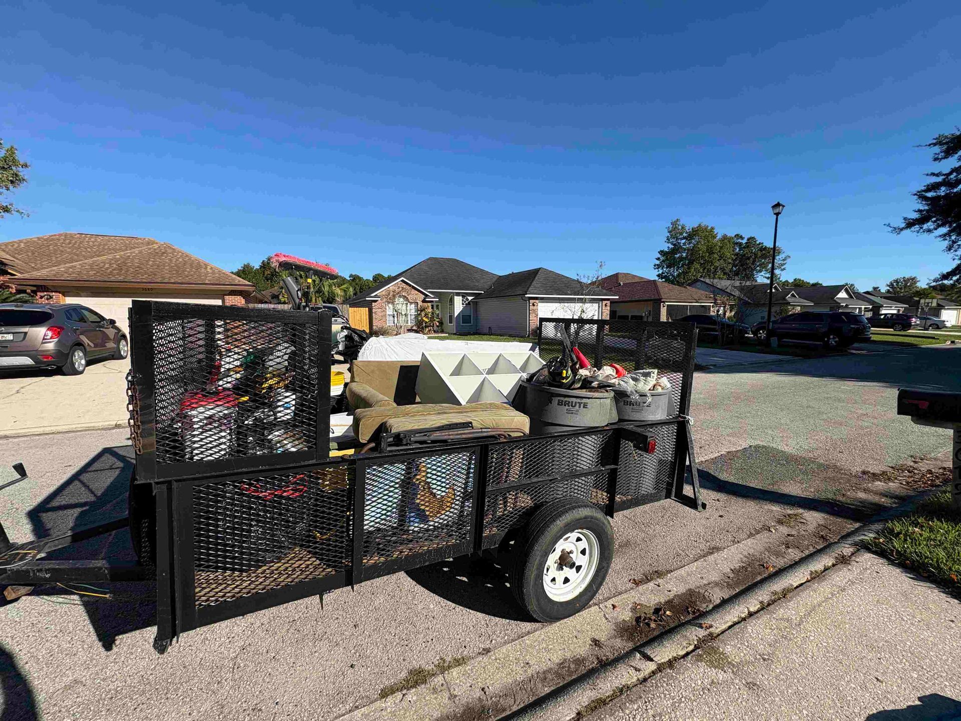 A trailer loaded with various items sits parked on a residential street under a blue sky.