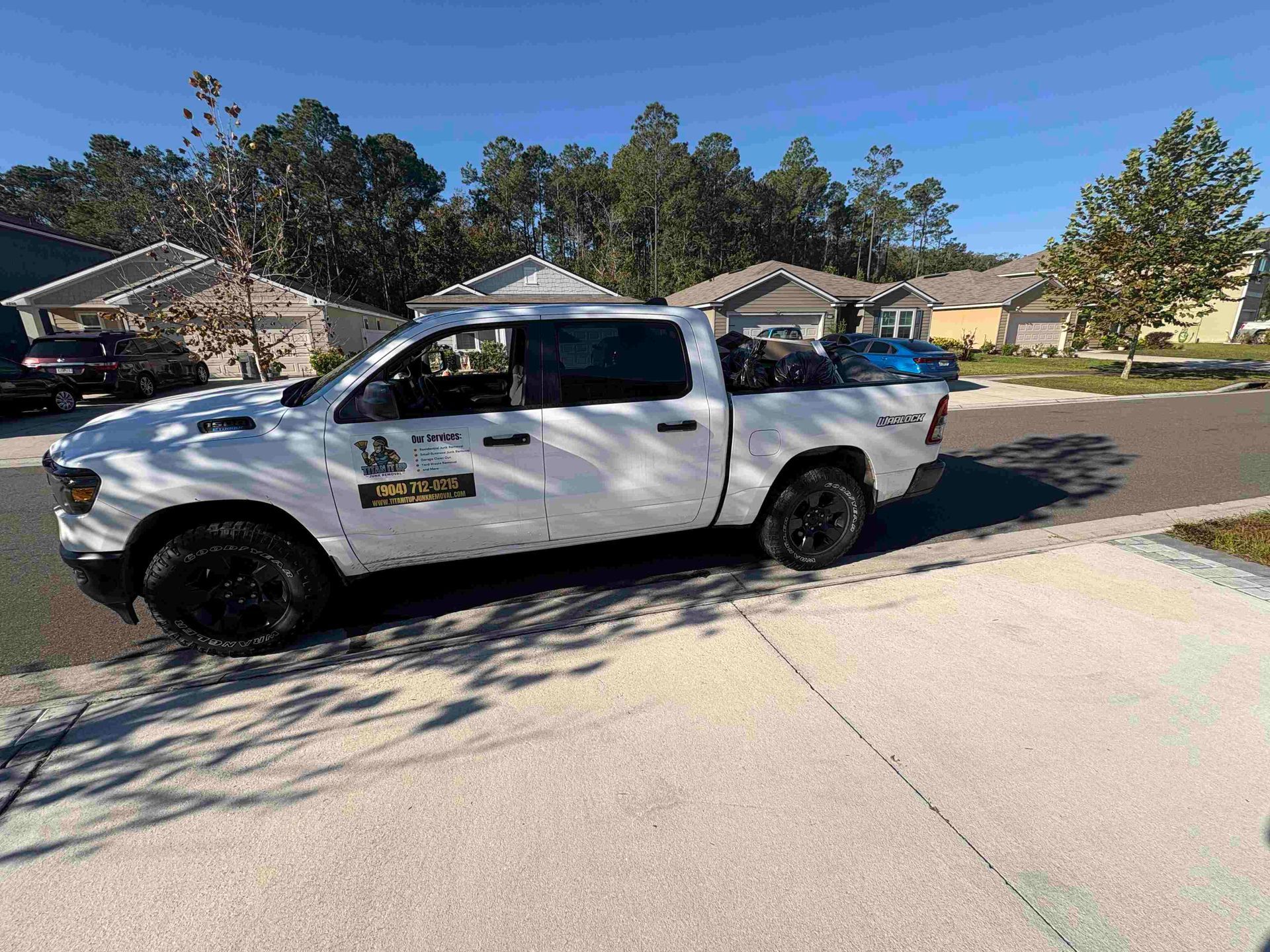 White pickup truck parked on a residential street; trees and houses in the background on a sunny day.