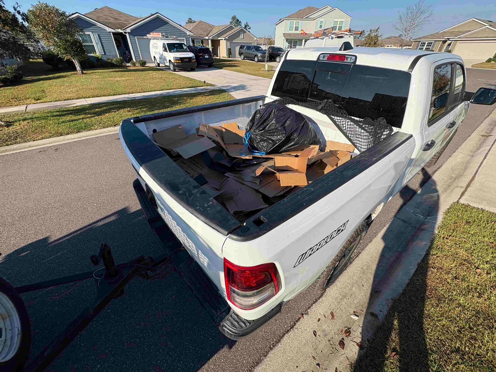 White pickup truck bed filled with cardboard boxes and a black trash bag, parked on the street.