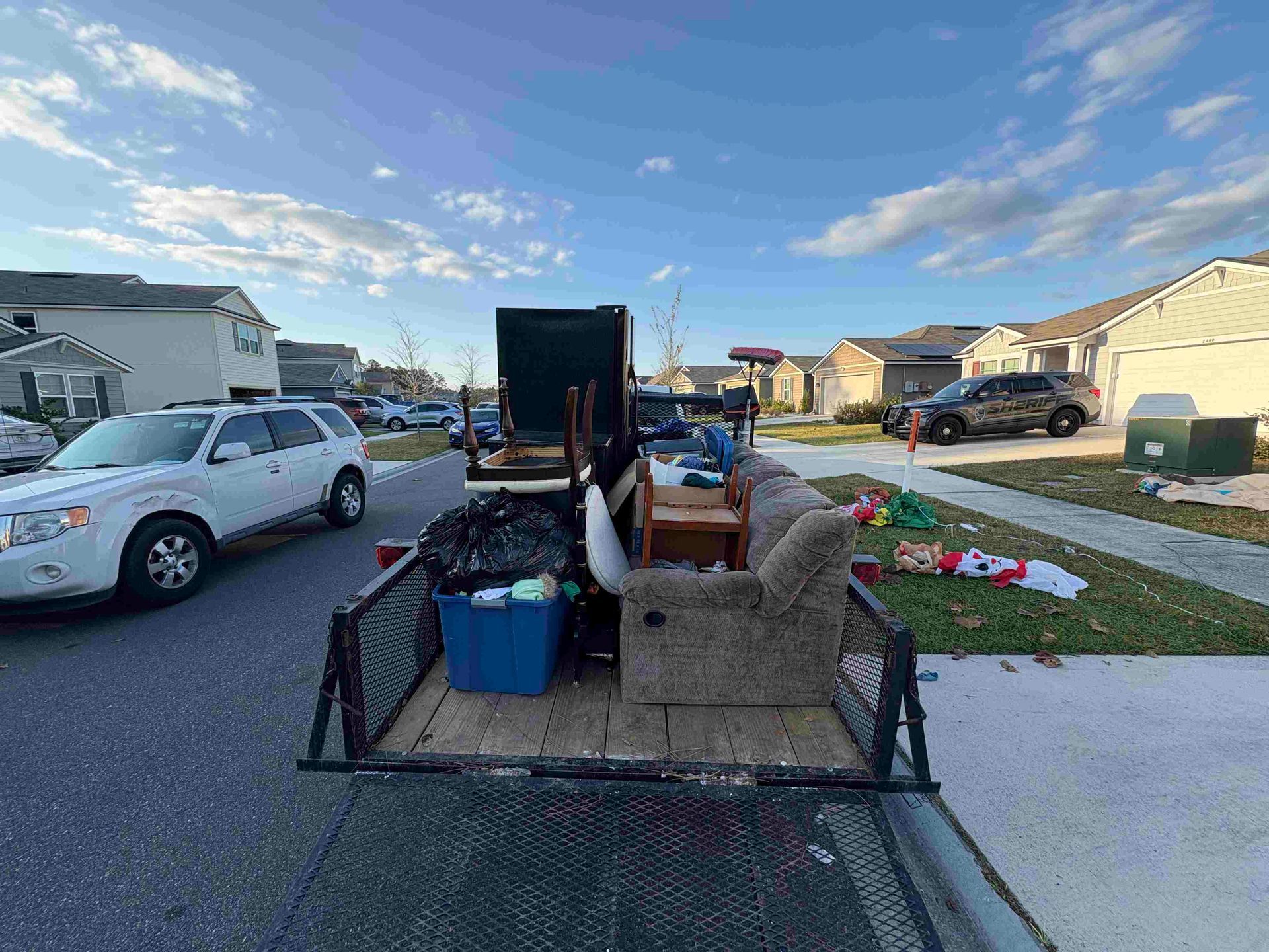 Trailer loaded with furniture and trash in a residential street; blue sky, cars parked.