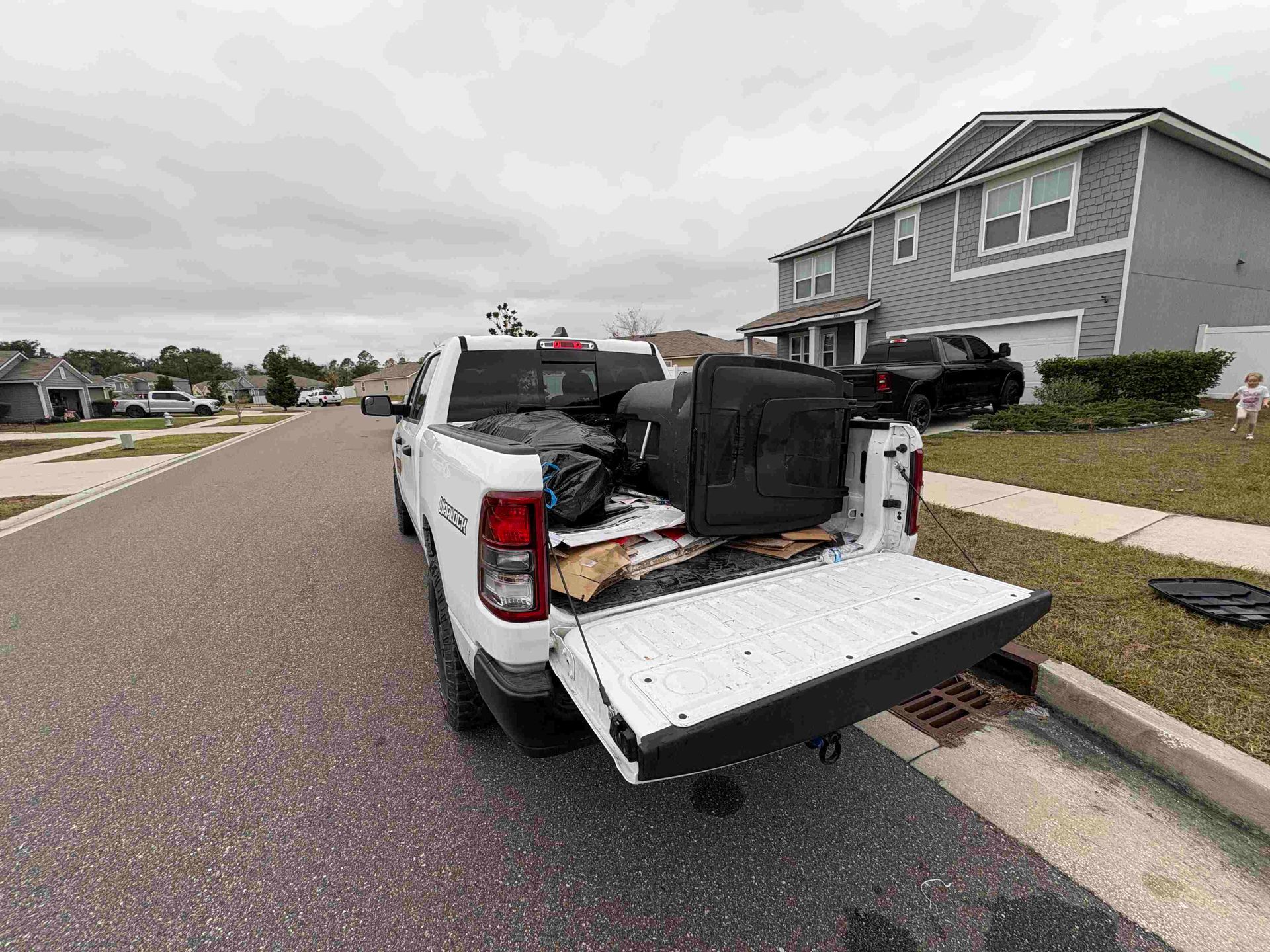 White pickup truck parked with open tailgate, loaded with items on a residential street. Cloudy sky.