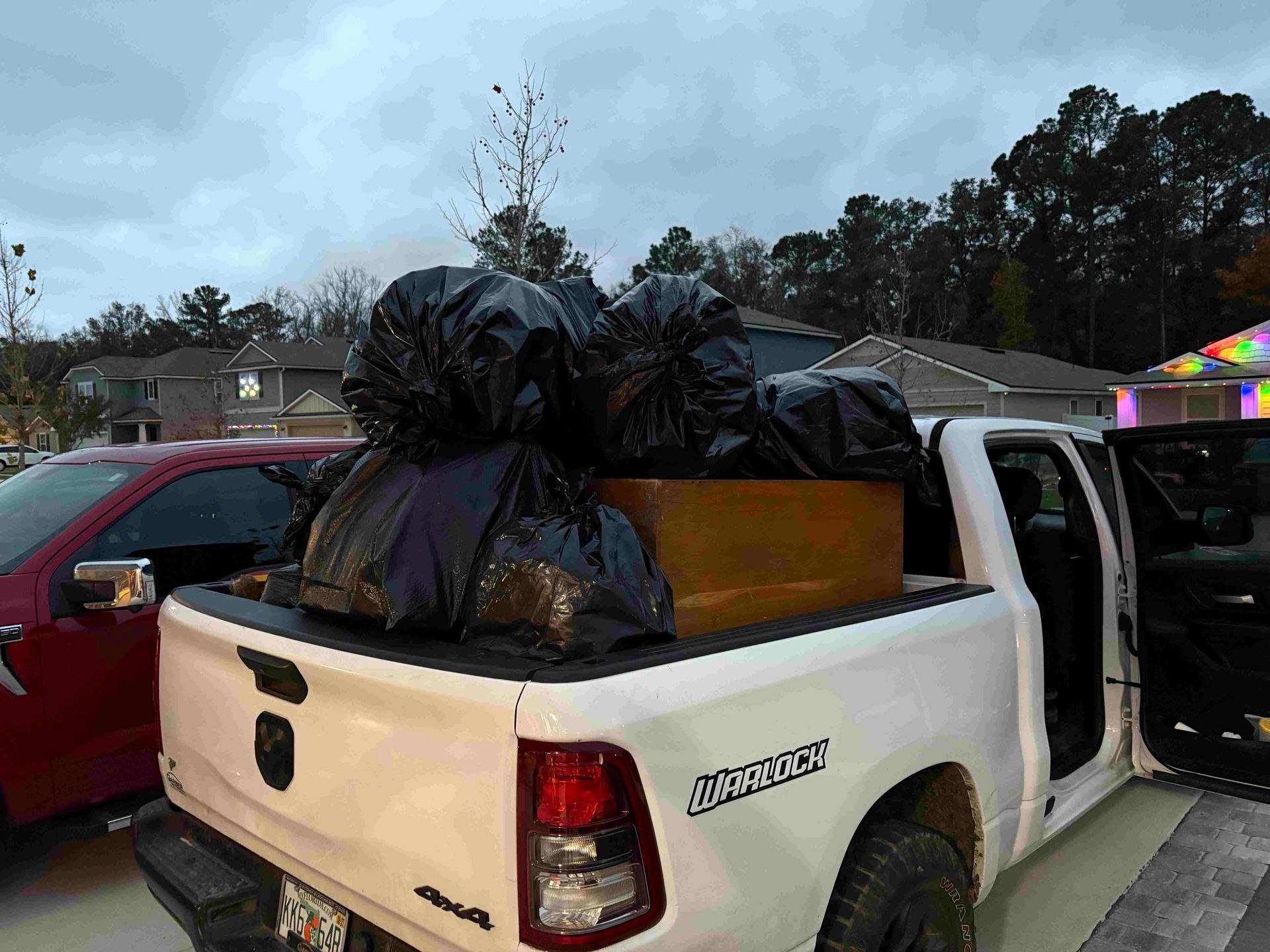 White pickup truck bed filled with black trash bags and a cardboard box; cloudy sky.