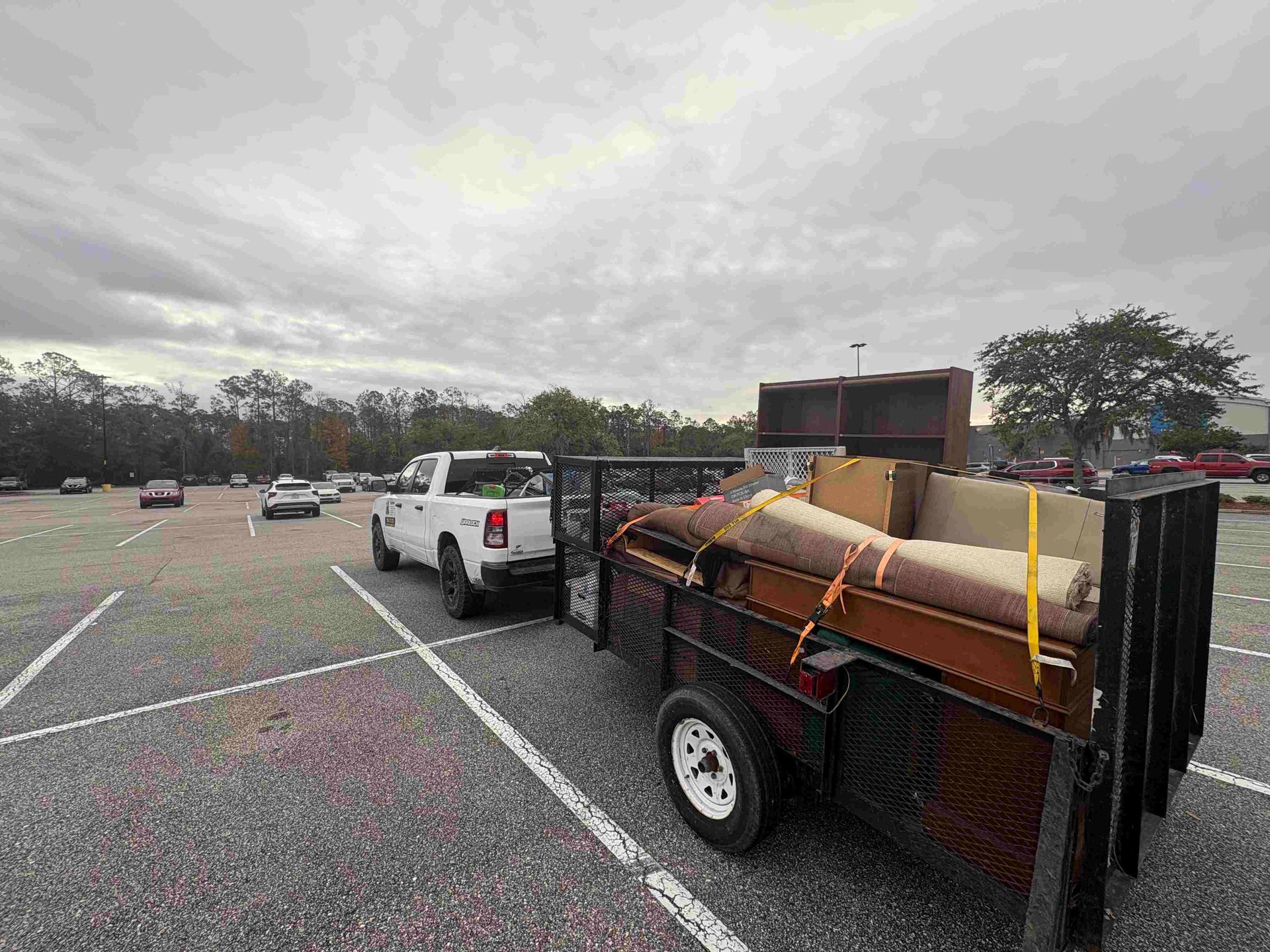 White truck towing trailer loaded with furniture in a parking lot on a cloudy day.