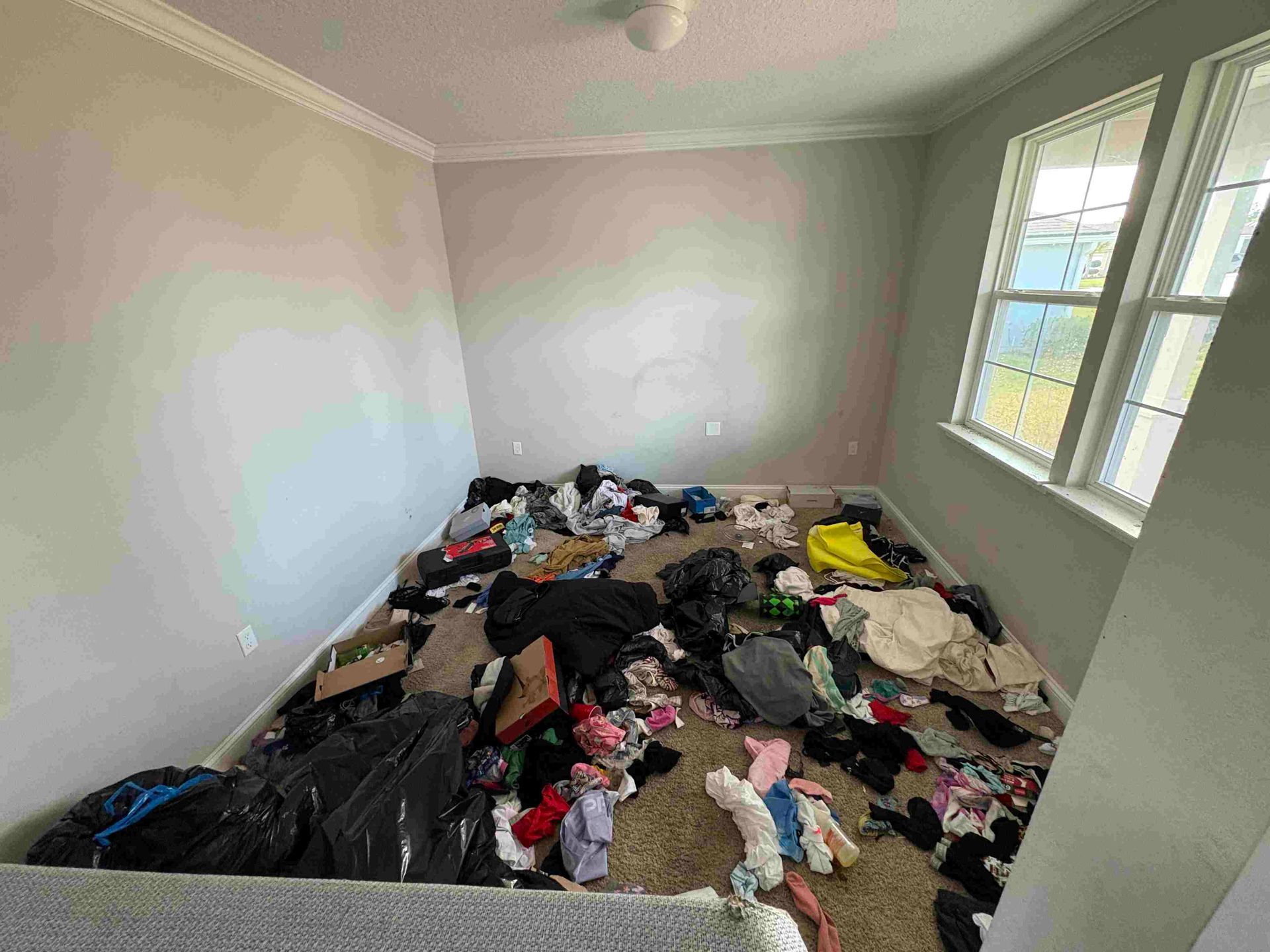 Room with a large pile of scattered clothing and trash on the floor. A window is in the corner.