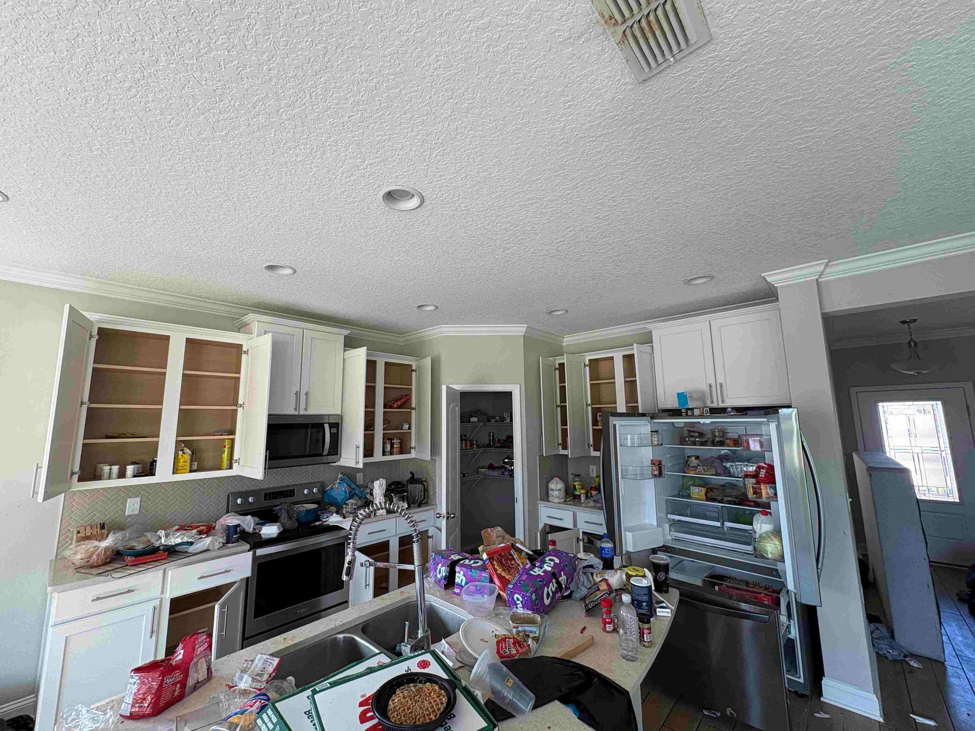 Messy kitchen with open cabinets, appliances, and clutter on countertops.