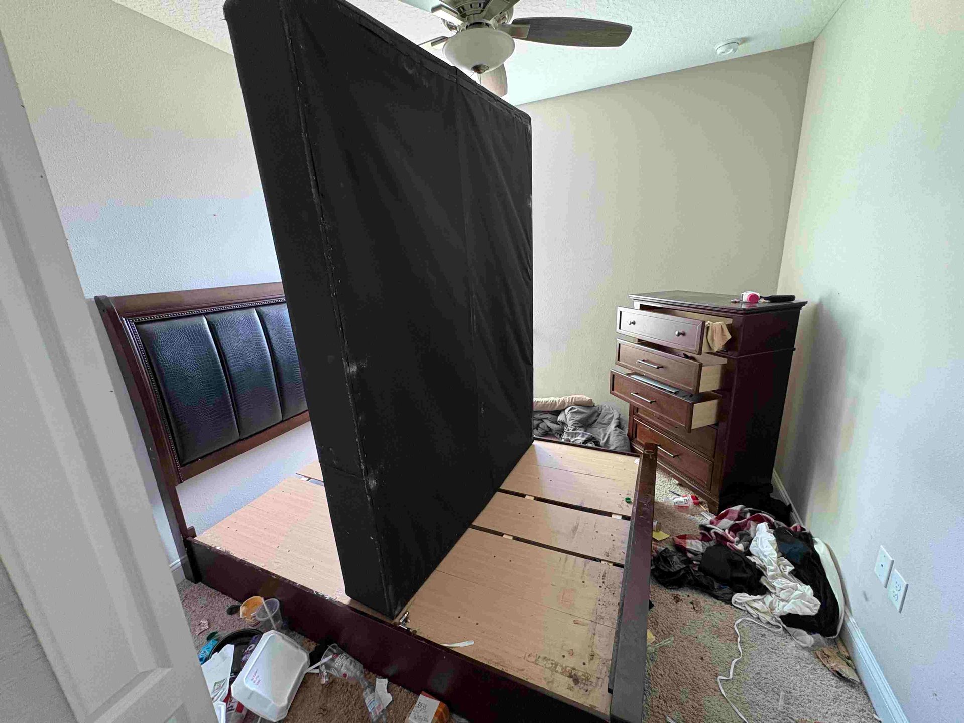 Bedroom with a dark headboard, mattress, dresser, and debris on the floor.