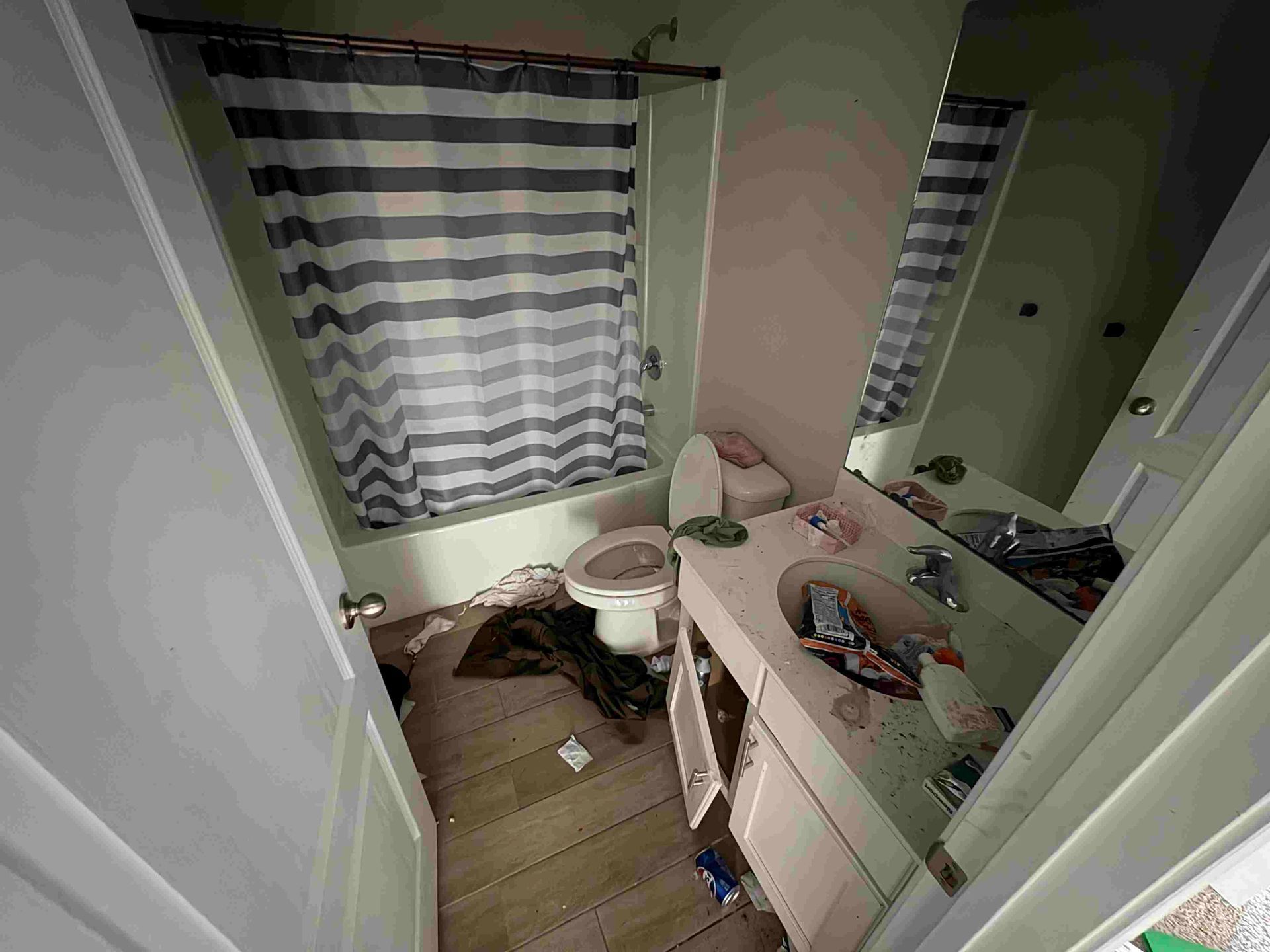 Bathroom with a toilet, sink, and shower. The space is cluttered, with debris on the floor.
