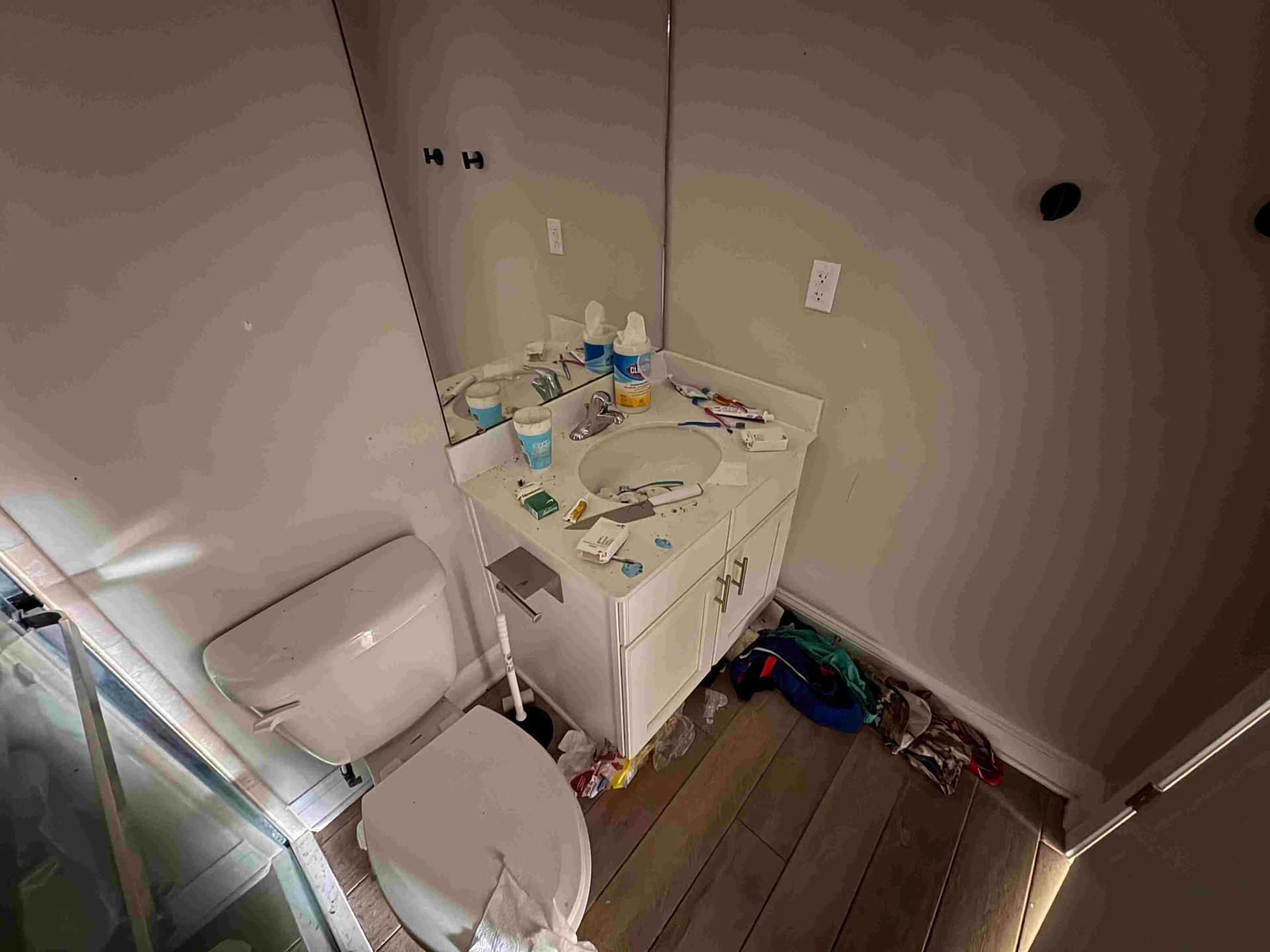 Bathroom with toilet, sink, mirror, and messy countertop.