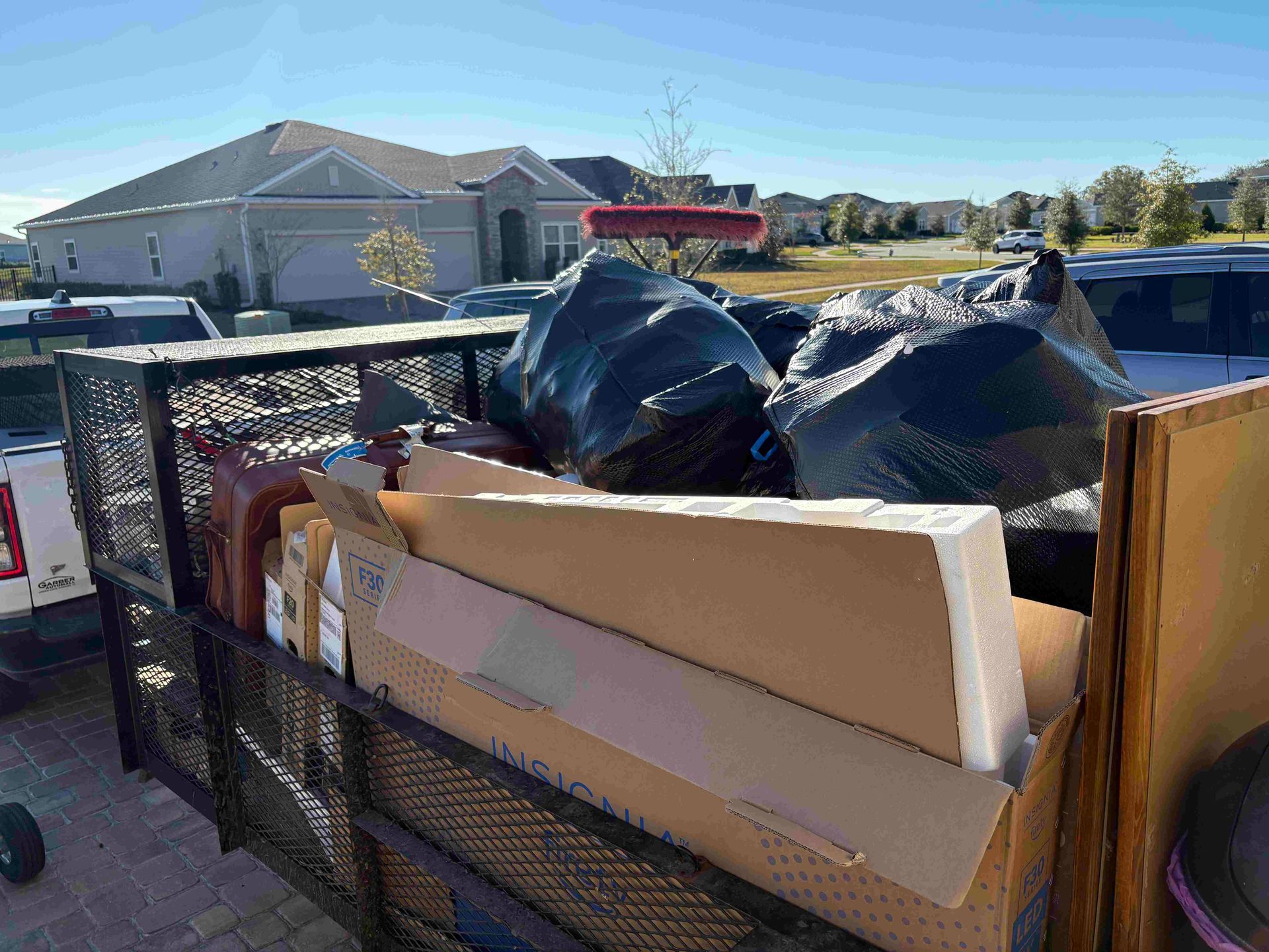 Trailer loaded with garbage bags, cardboard, and construction materials in a residential area on a sunny day.