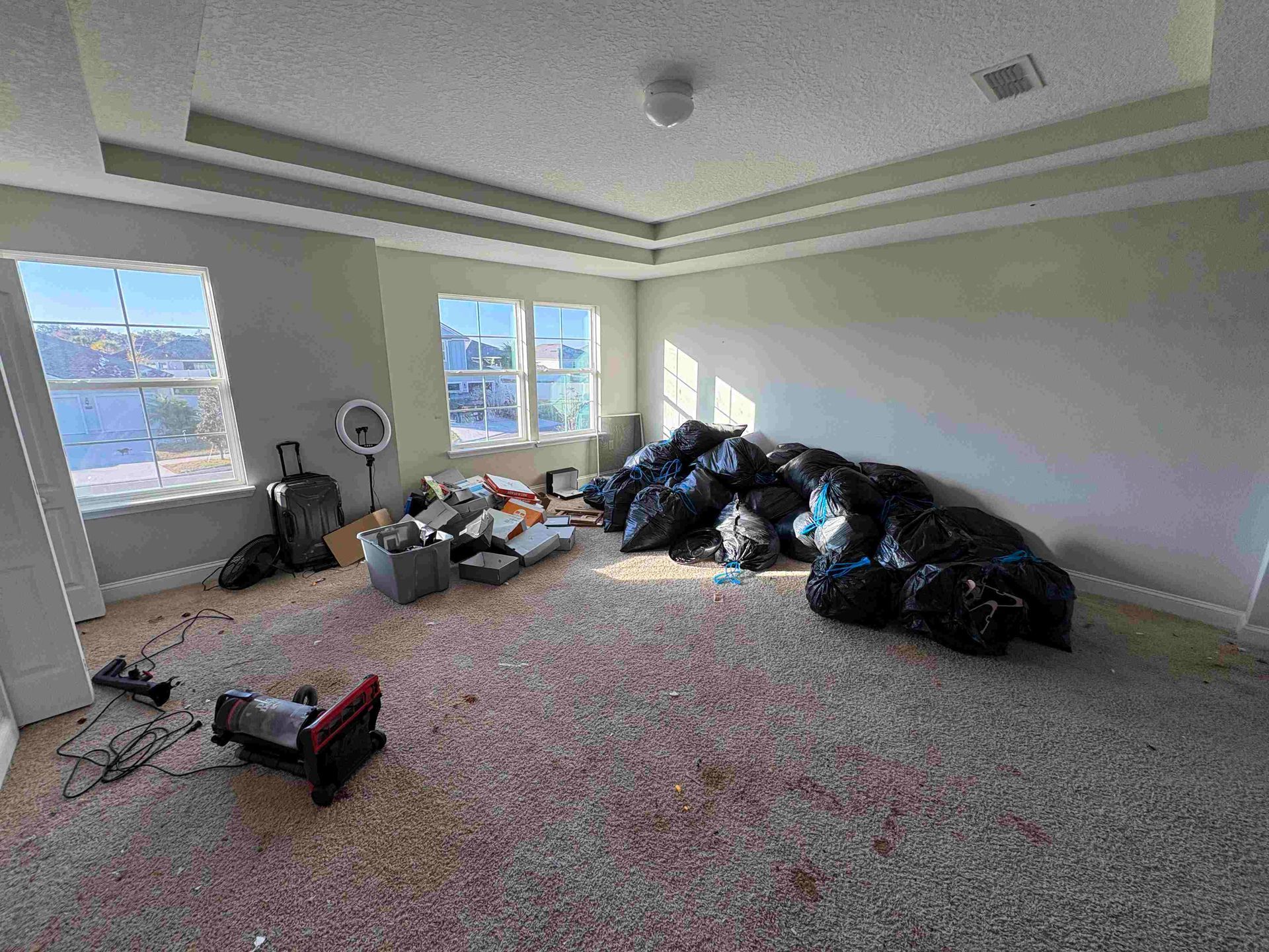 Room with debris and black trash bags; windows and ceiling details are visible.