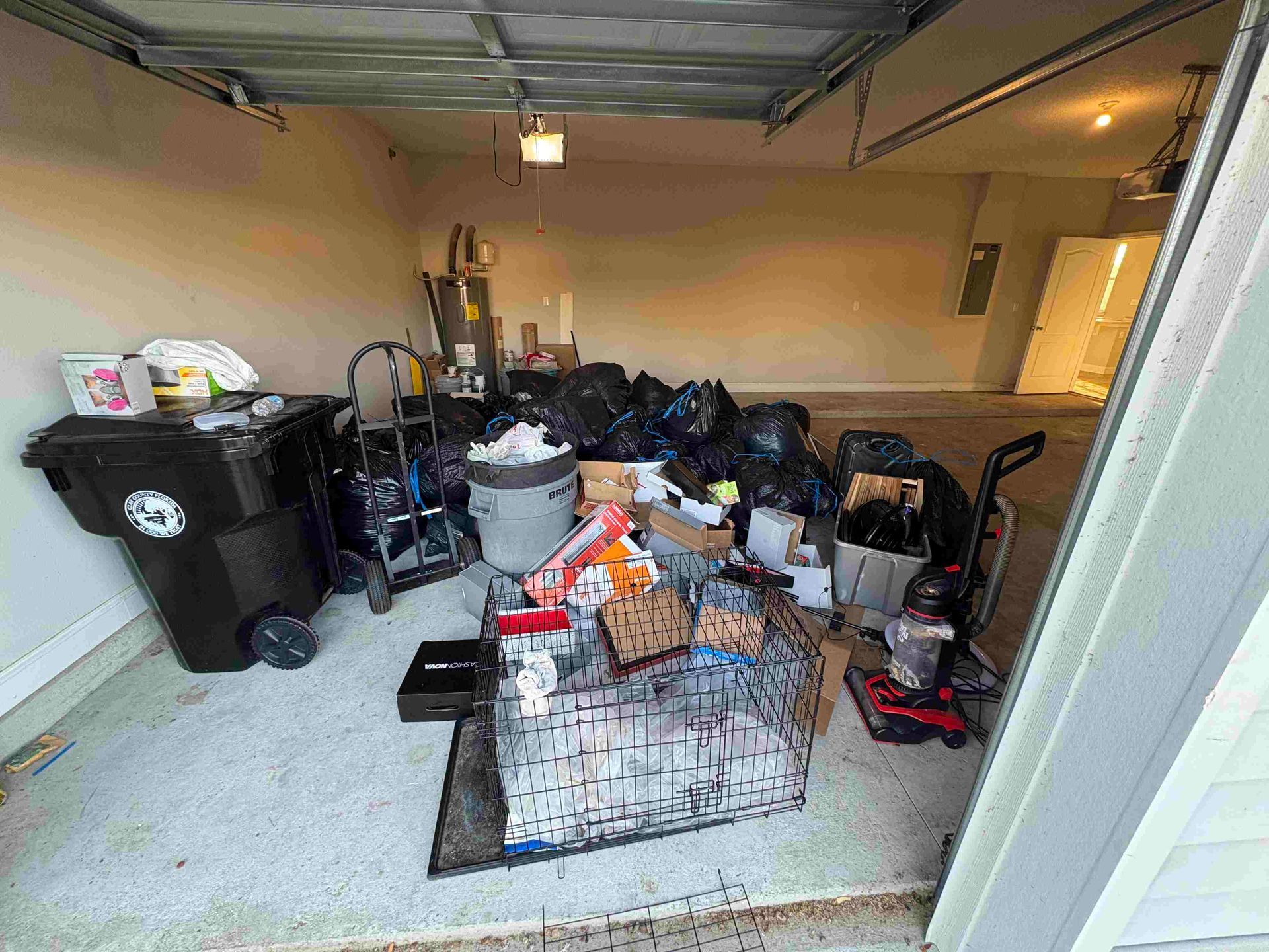Cluttered garage with trash bags, a trash can, and various items.