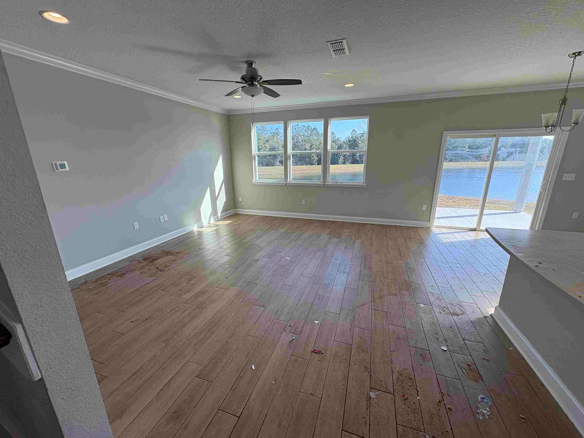A living room with hardwood floors, windows, and a ceiling fan; natural light illuminates the space.